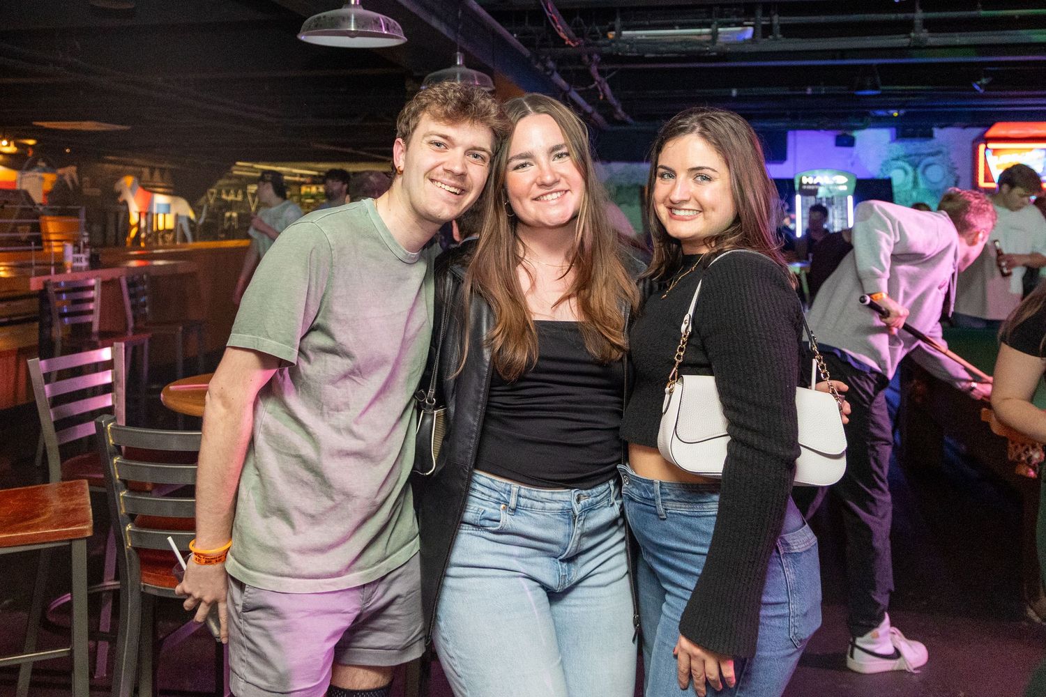 Three friends enjoying a night out together at a dimly lit bar with purple lighting in the background.