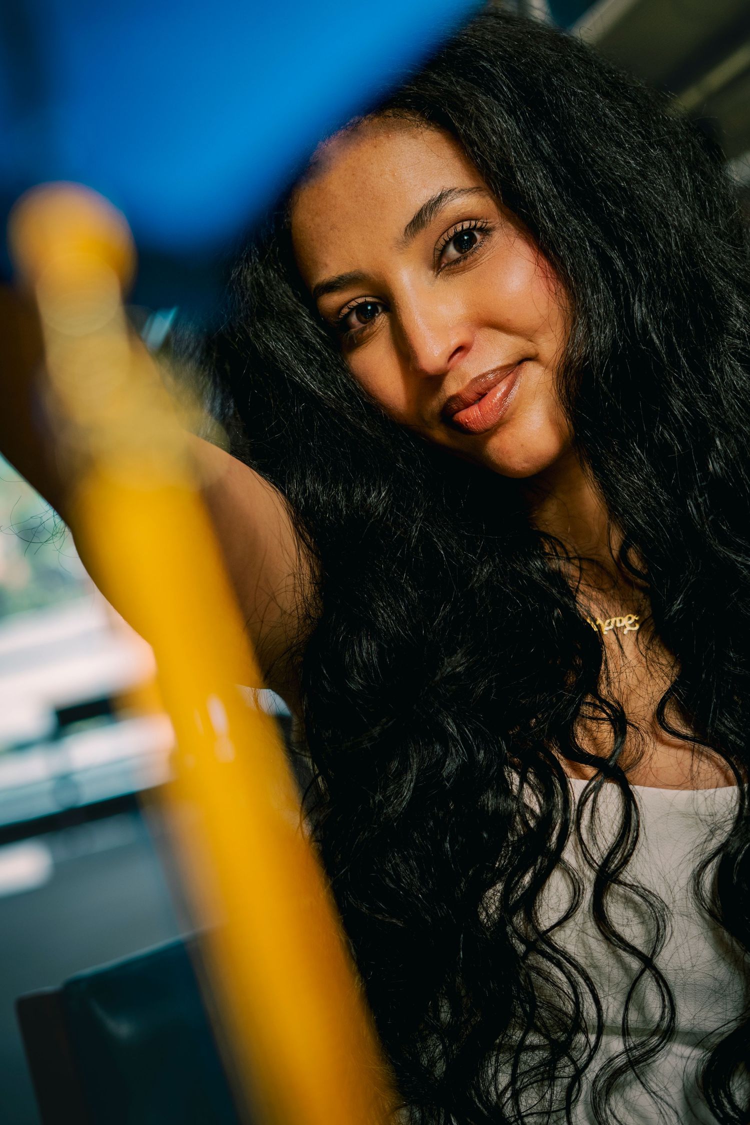 A portrait series showing long dark curly hair against a blurred blue background with a yellow accent in frame.