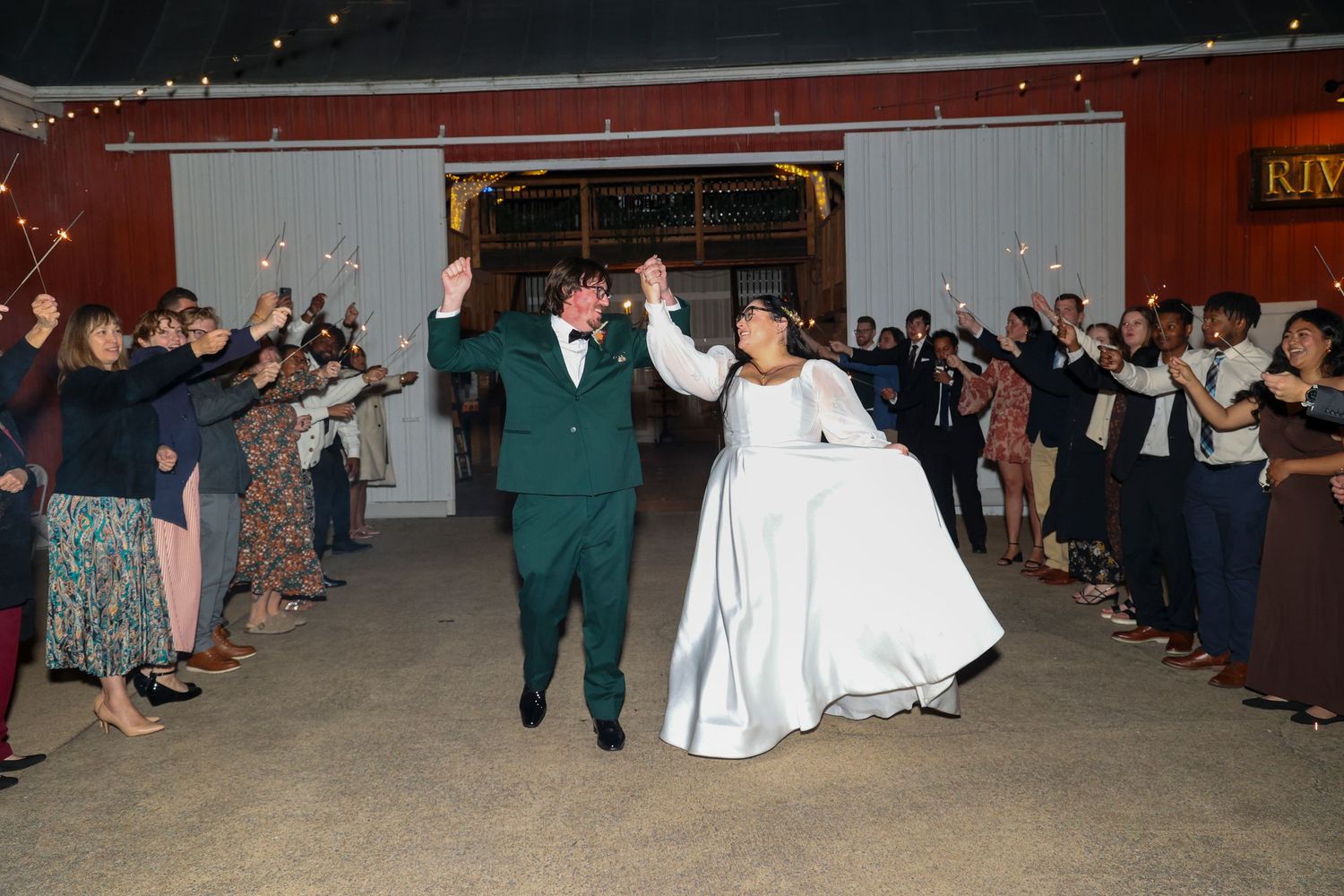 Wedding guests form a line on the dance floor during a reception celebration at a rustic red barn venue.