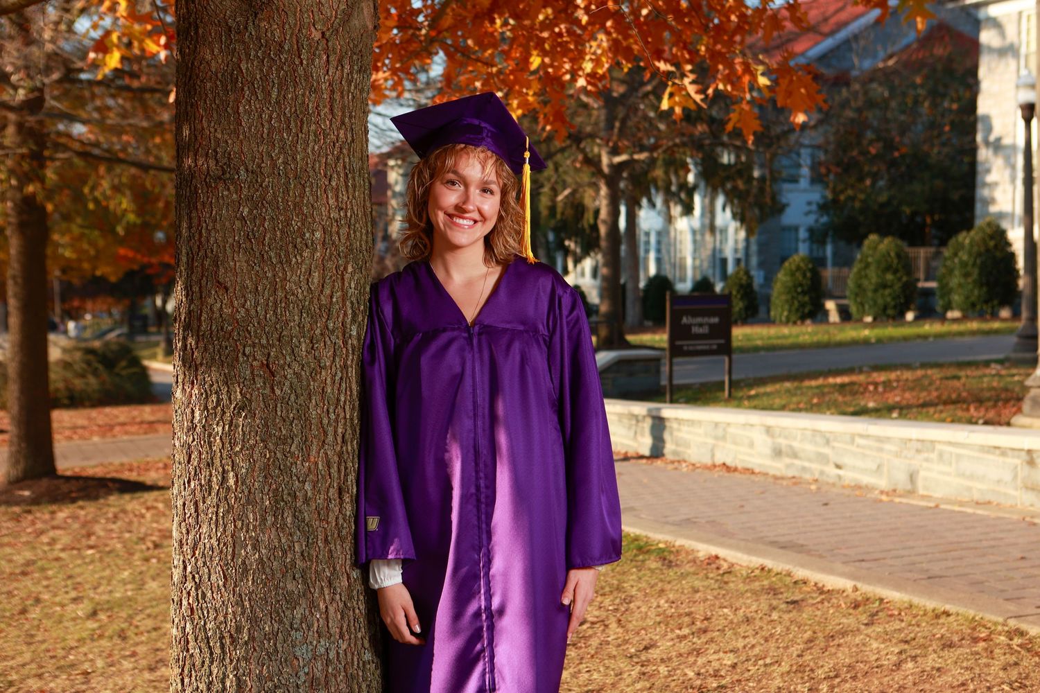 A series of five outdoor photos showing someone in a purple graduation gown posing near autumn trees on a college campus.