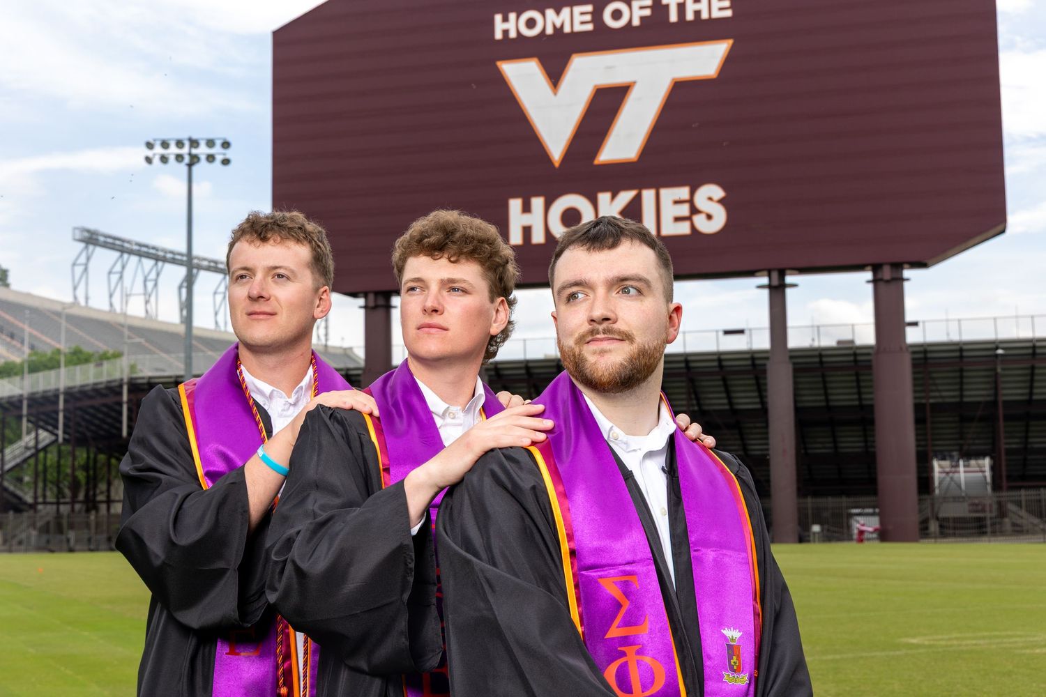 Football players stand together wearing pink jerseys on a practice field with Virginia Tech signage in the background.