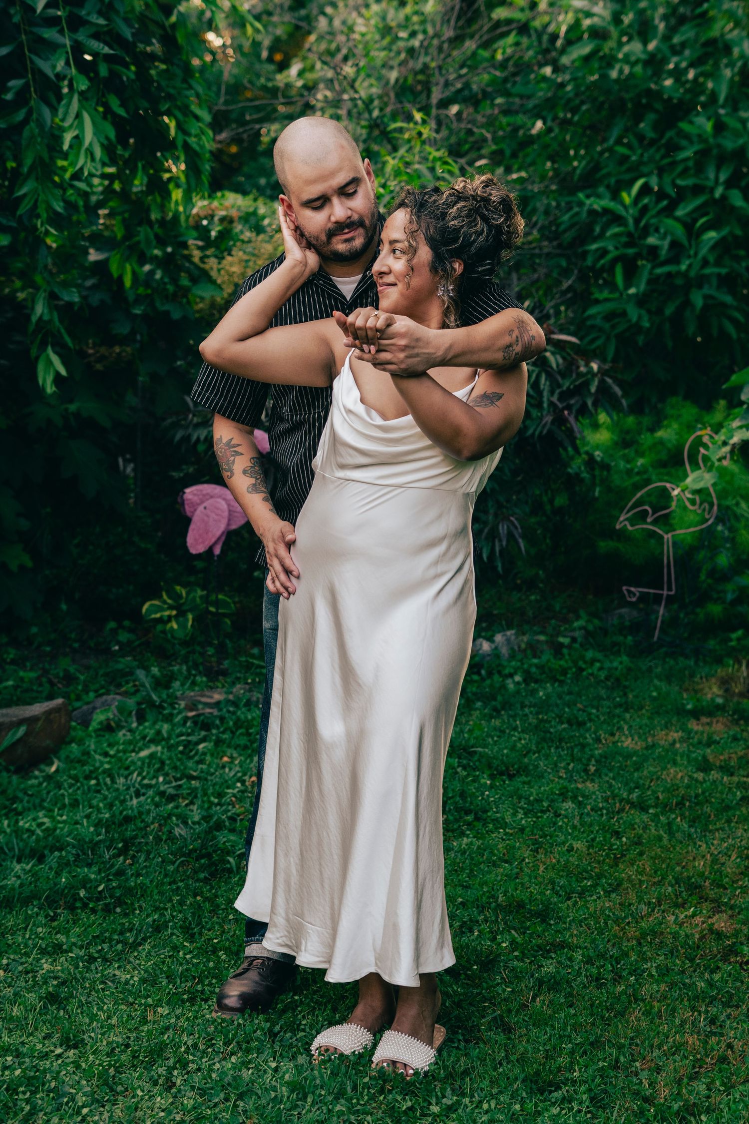 Two people share a tender embrace while dancing together in a lush garden setting.