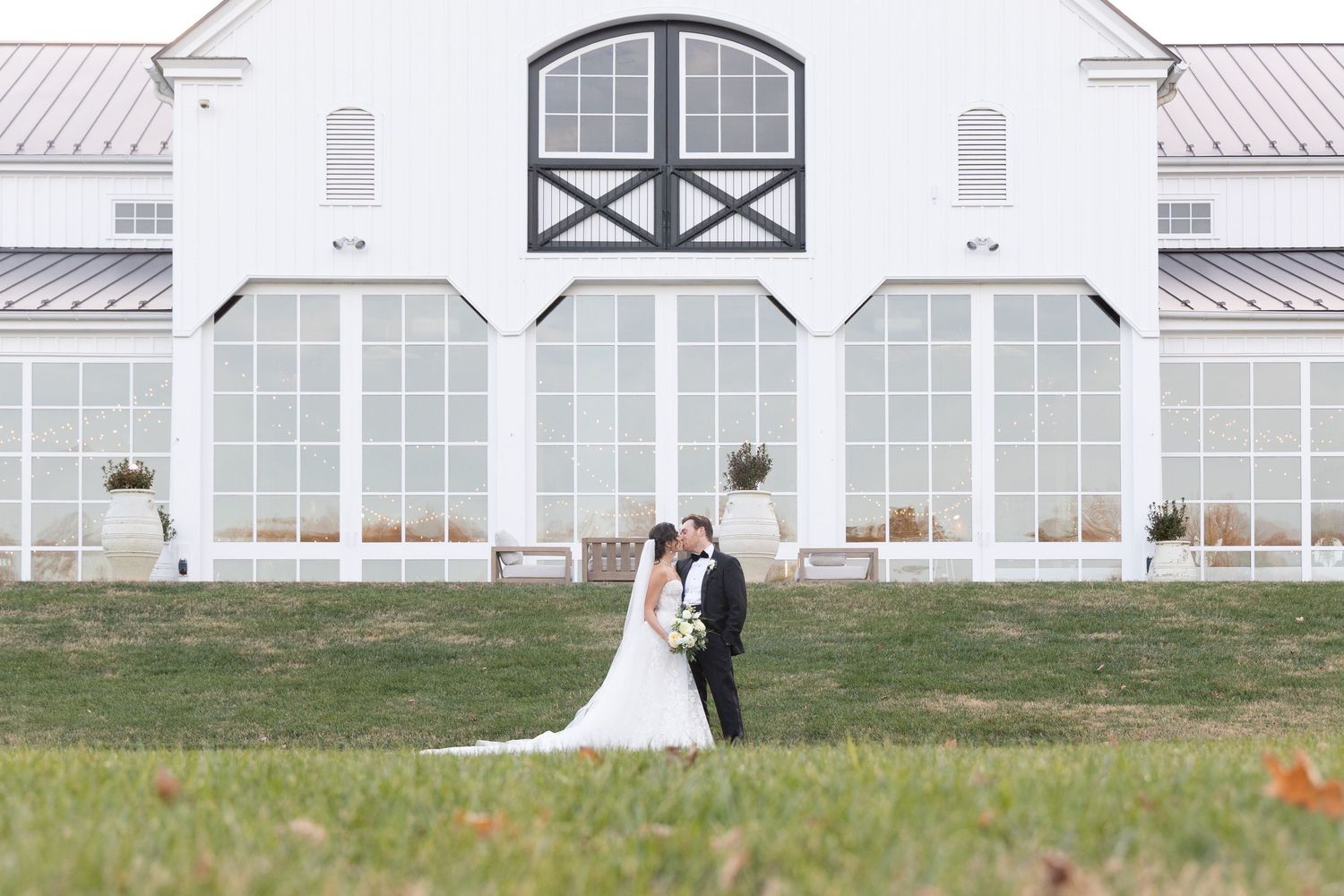 A series of wedding photos showing a couple in front of a white barn and greenhouse venue on their special day.