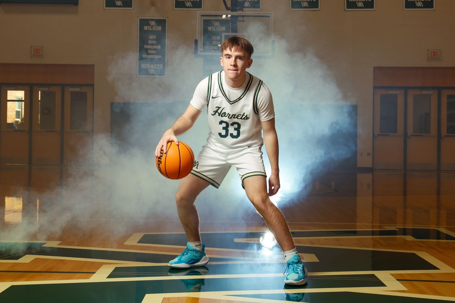 Basketball player in white jersey posing with dramatic smoke effects in gymnasium.