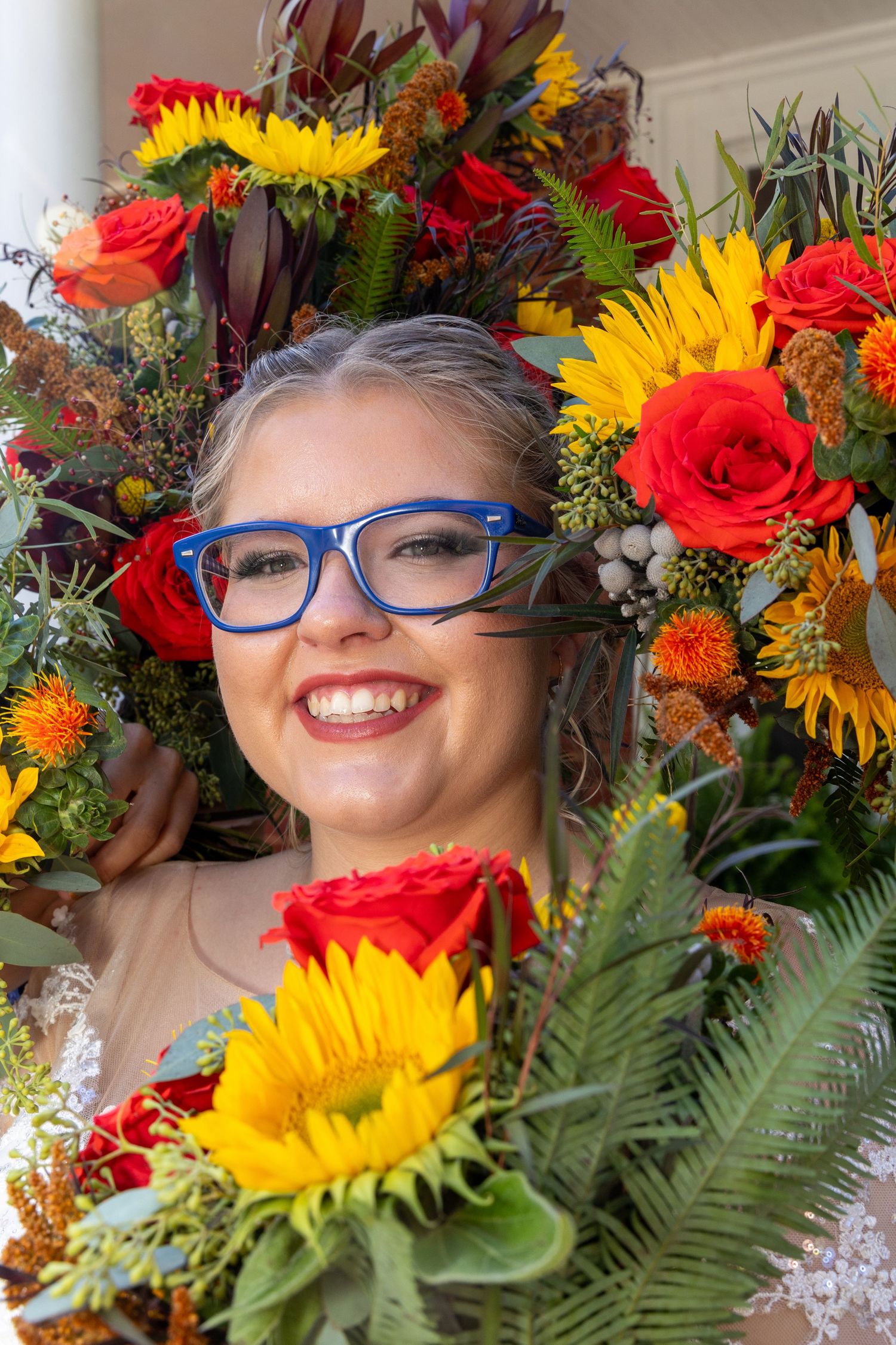 Vibrant floral arrangement with sunflowers, red roses and orange blooms surrounded by lush green foliage.
