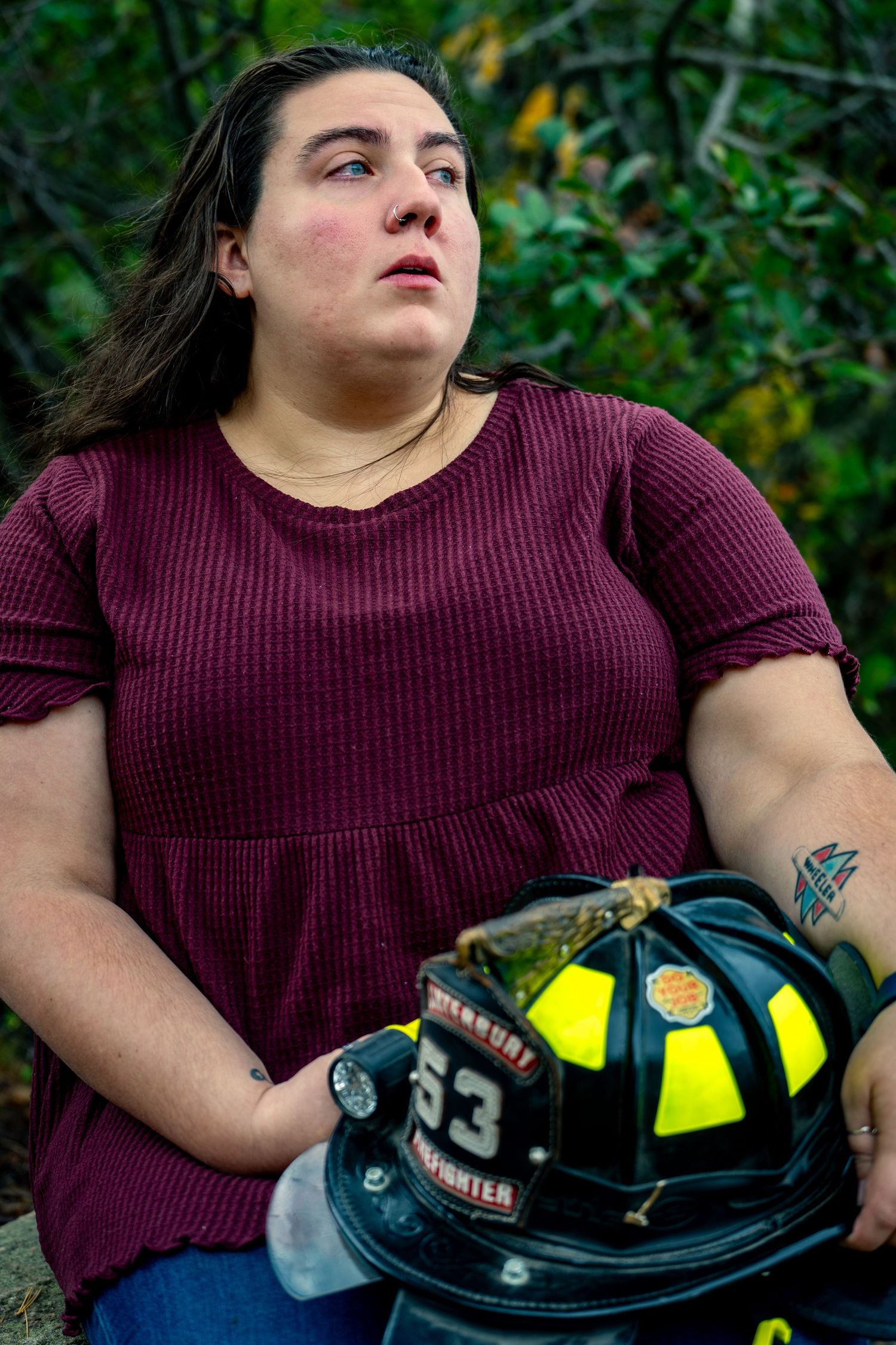 A person in a maroon sweater holds a firefighter helmet while sitting outdoors.