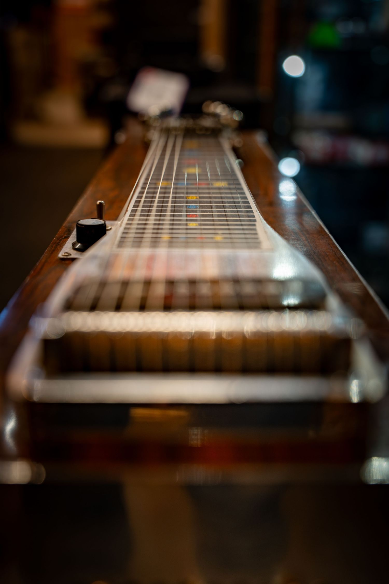 Vintage pedal steel guitar with colorful fret markers displayed on a dark background in a music store.