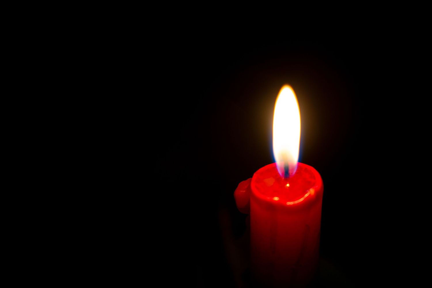 A glowing red candle with a bright flame illuminates the darkness against a black background.
