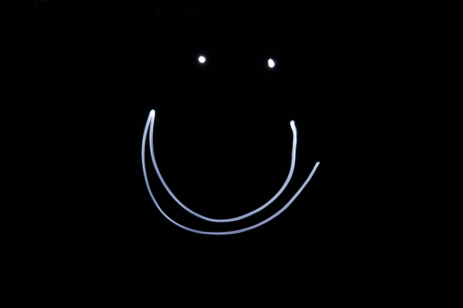 Glowing light painting smiley face with bright eyes and curved smile on black background.