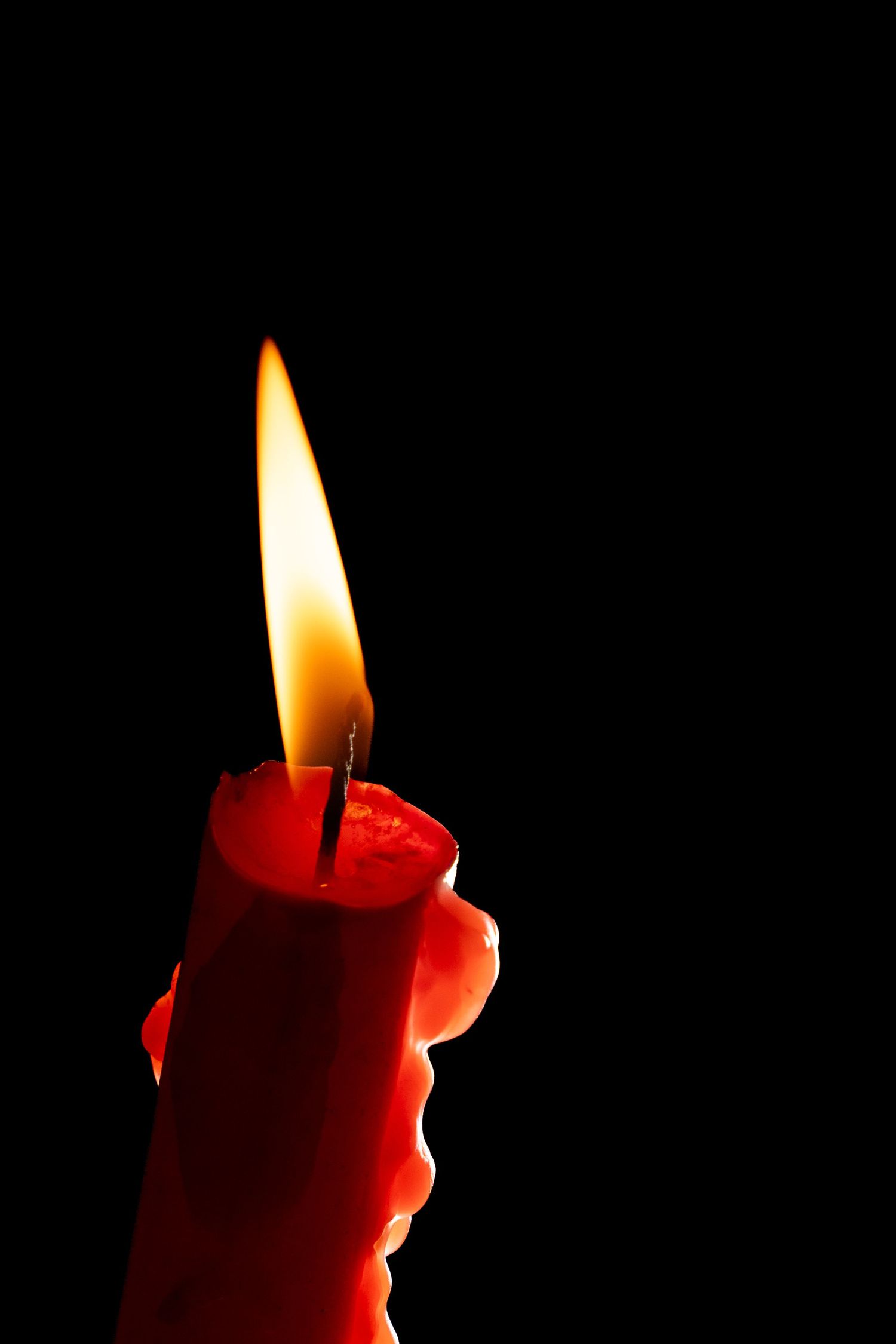 A hand holding a lit red candle with glowing flame against a dark black background.