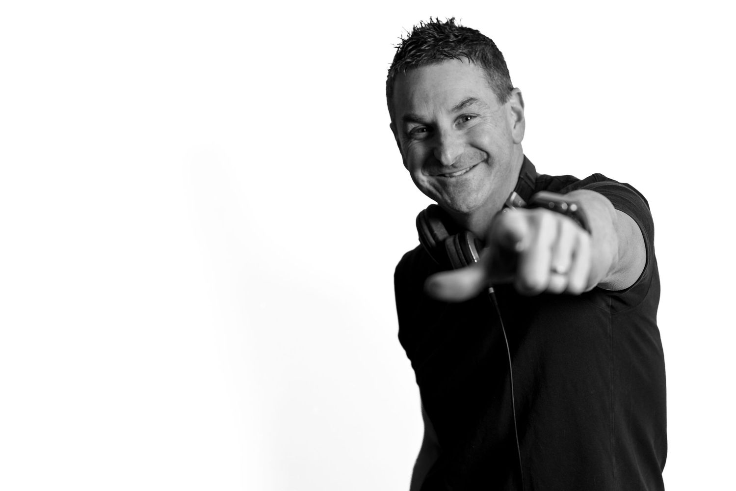 Smiling man in black shirt pointing at camera in black and white portrait photo.