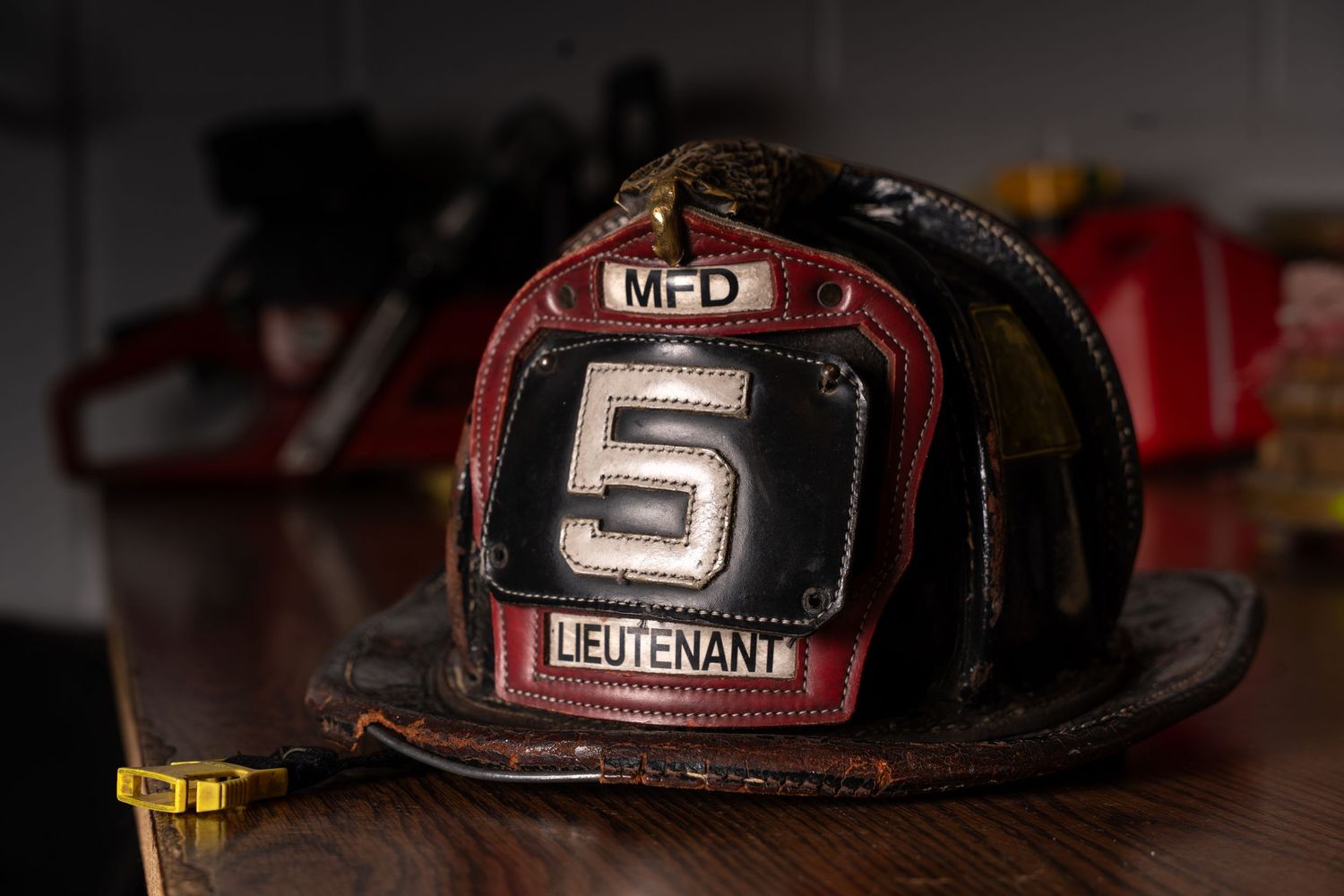 Vintage black leather MFD Lieutenant fire helmet with number 5 badge displayed on wooden surface in firehouse.