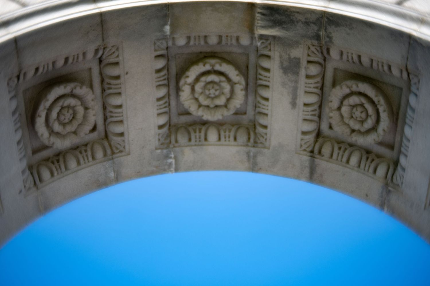 Ornate stone arch detail with carved rosette decorations against bright blue sky.