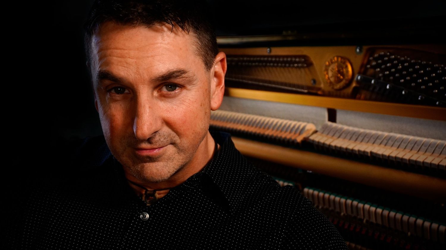 Professional musician sits at a grand piano keyboard in a recording studio setting.