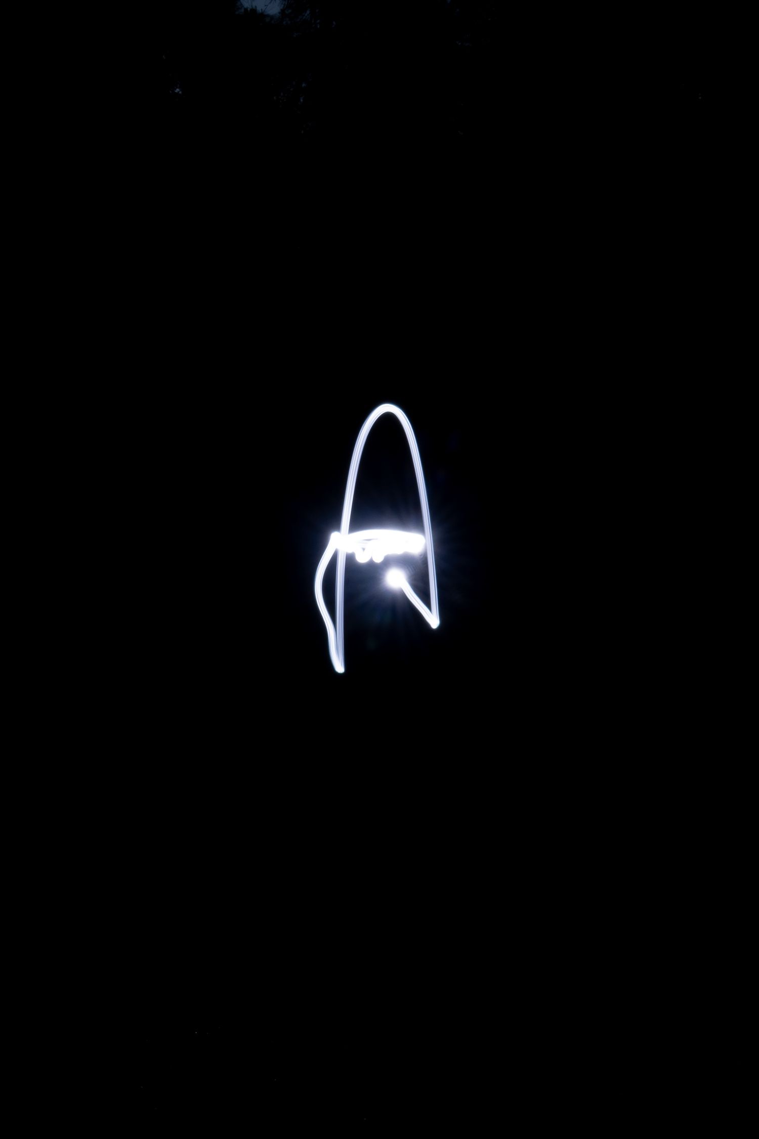 Light painting photography showing a glowing white rocket shape drawn with light against a dark black background.