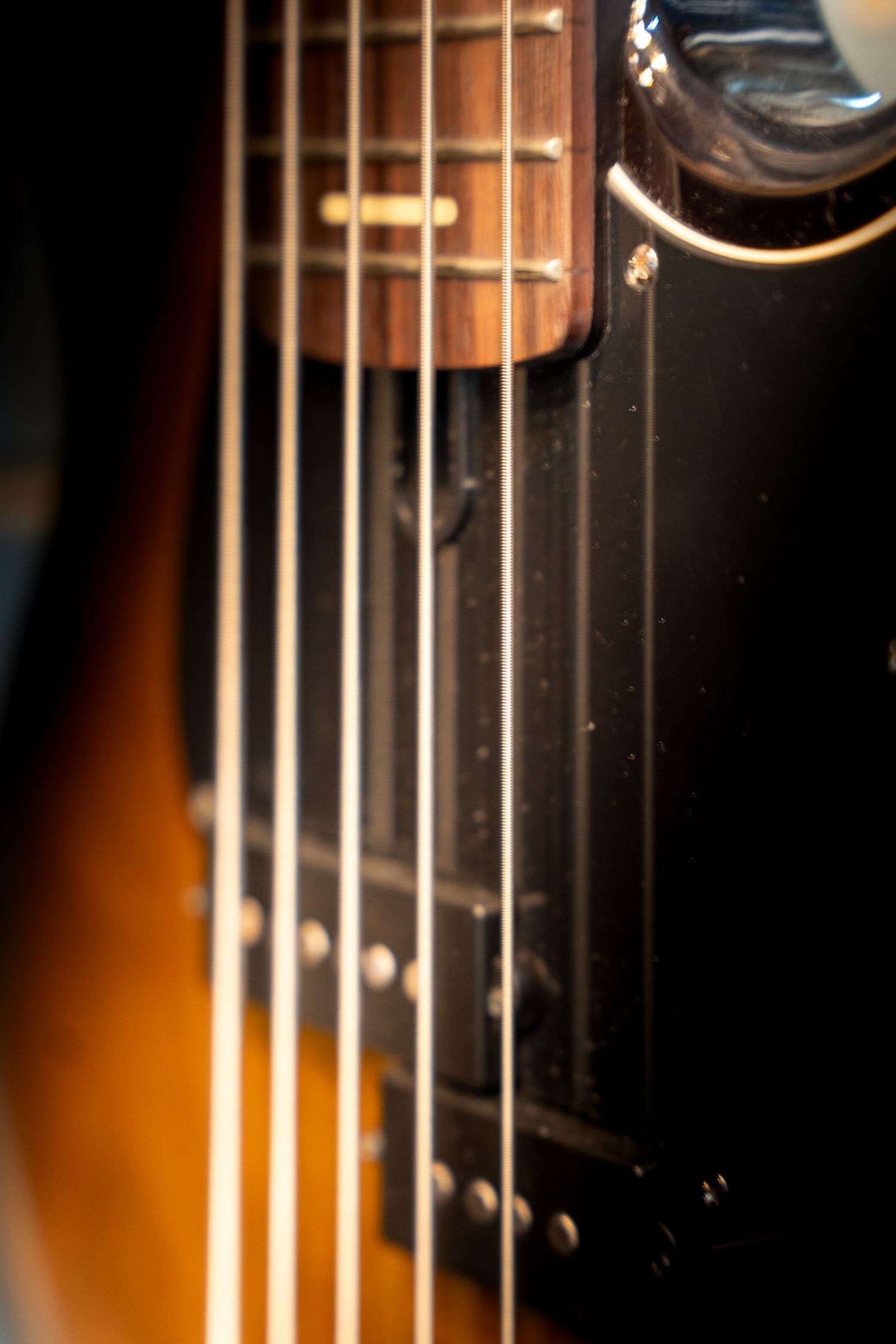 Close-up of electric guitar strings and fretboard with sunburst finish.