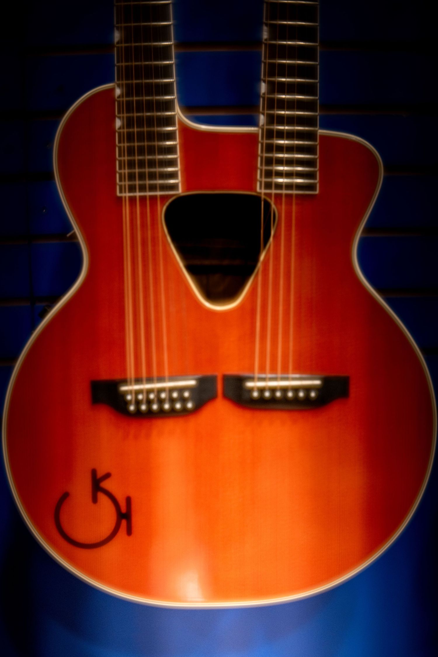 Unique double-neck acoustic guitar in cherry red finish with dual soundholes displayed against blue background.