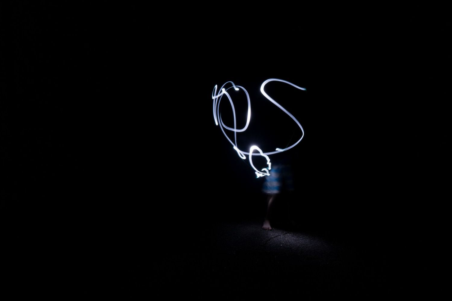 Person creating light painting art with glowing blue swirls against a dark black background in long exposure photography.