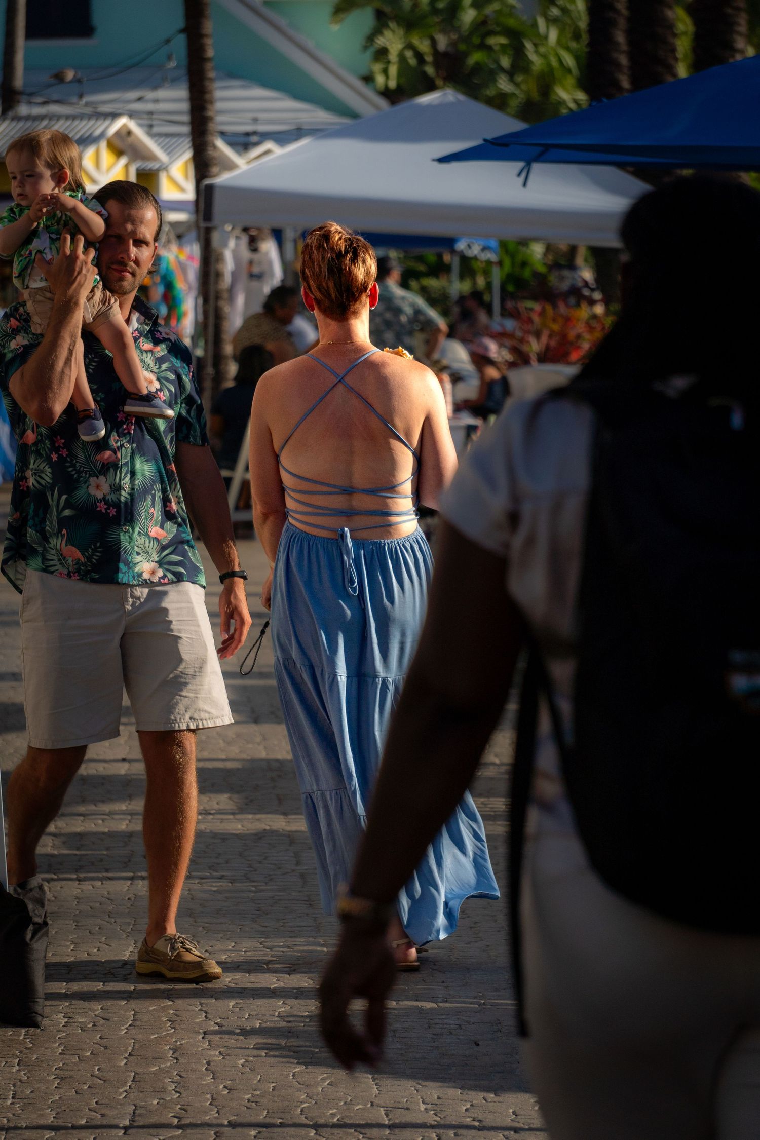 People walking on a cobblestone street with white market umbrellas and vendor tents visible in the background.