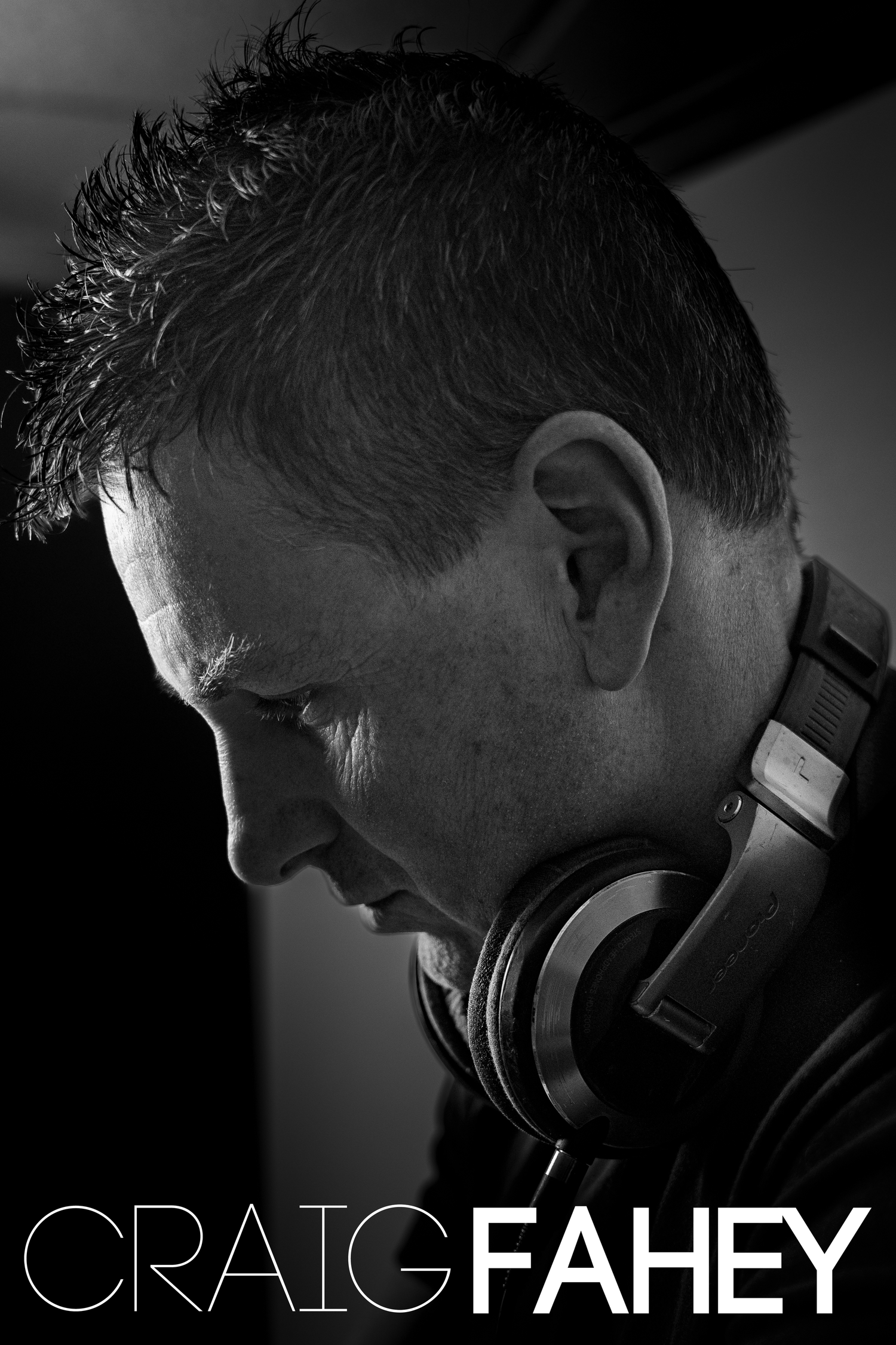 Black and white profile photo of DJ Craig Fahey wearing headphones around his neck, looking downward.