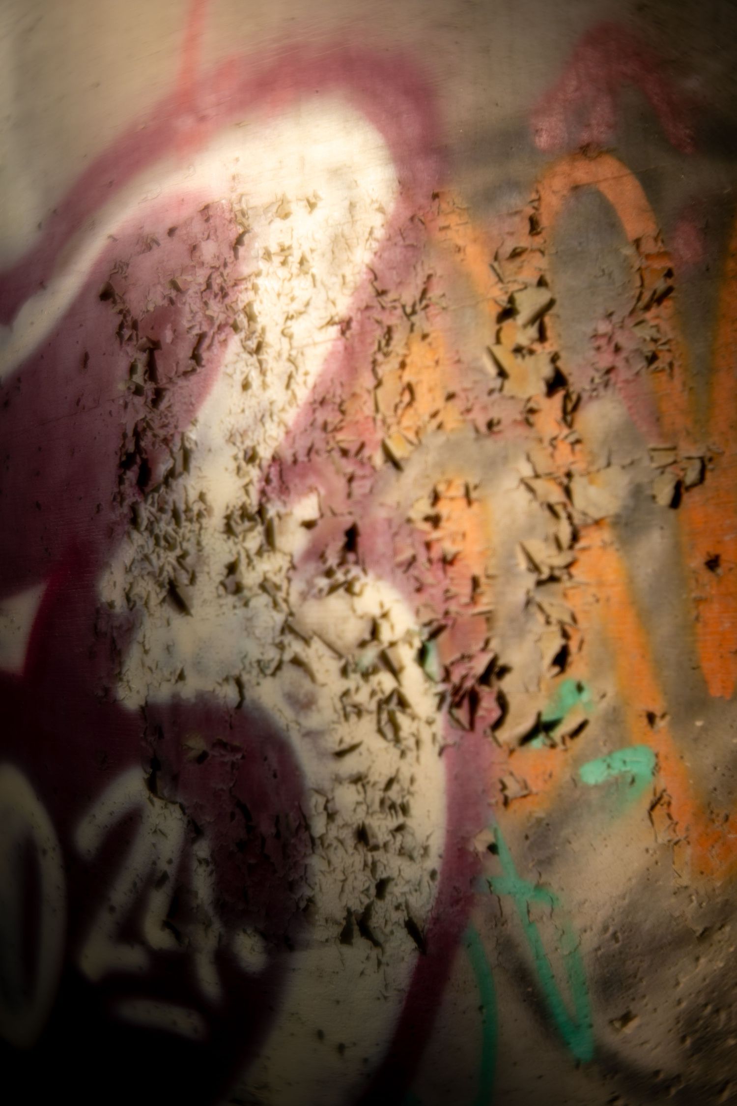 Abstract graffiti art on a weathered wall with pink, orange, and teal spray paint over peeling texture.
