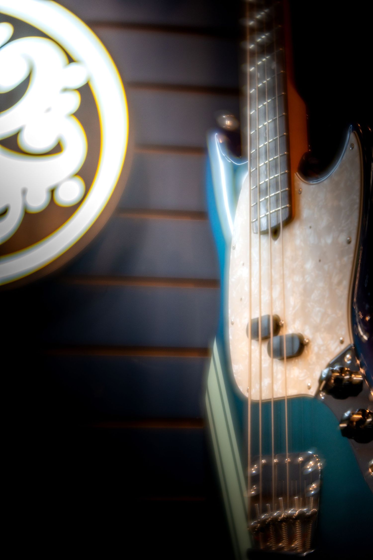 Close-up of a teal electric guitar with pearl pickguard leaning against a wood panel wall near an amplifier logo.