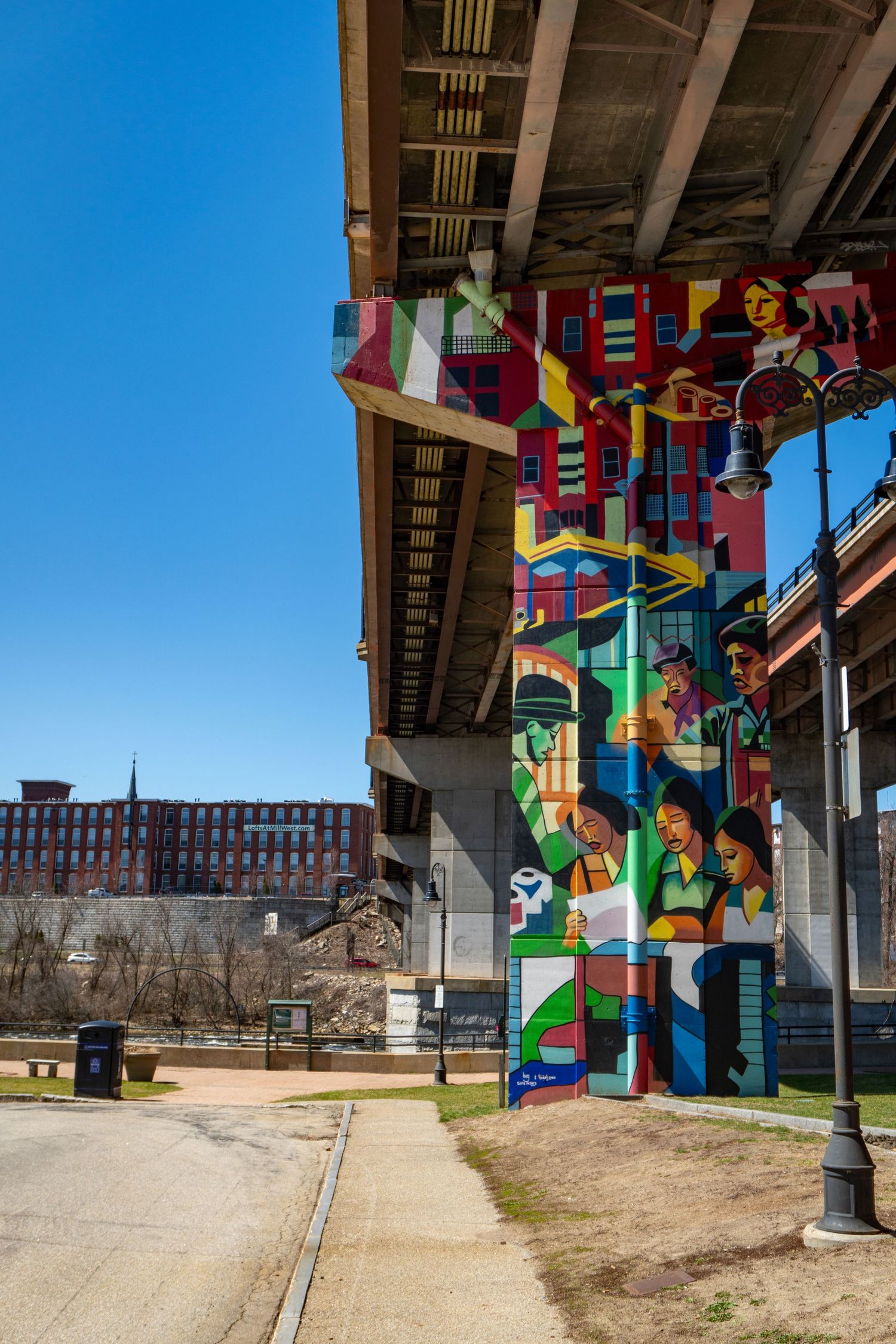 Colorful geometric murals painted on concrete bridge support columns with an industrial building visible in the background.