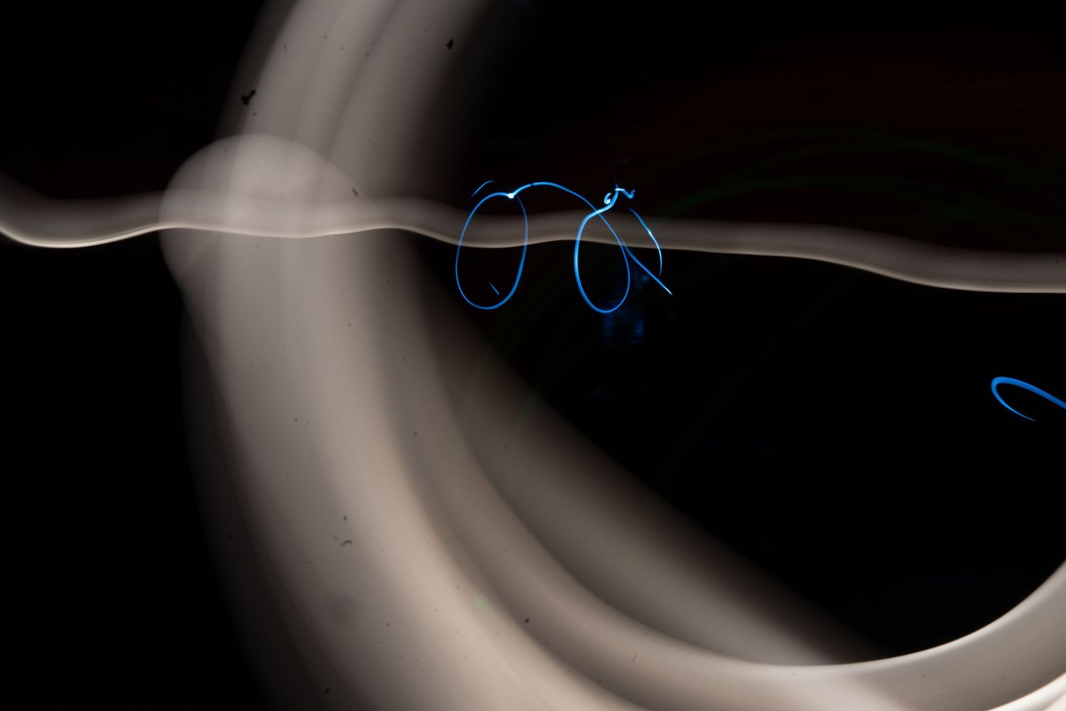 Abstract long exposure light painting with glowing blue loops and white smoke trails on a dark background.