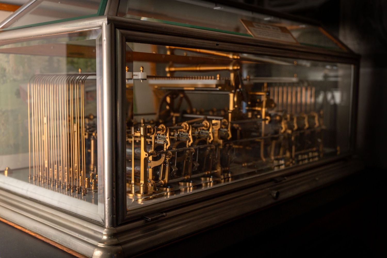 Intricate antique mechanical music box with brass components displayed under a glass case.