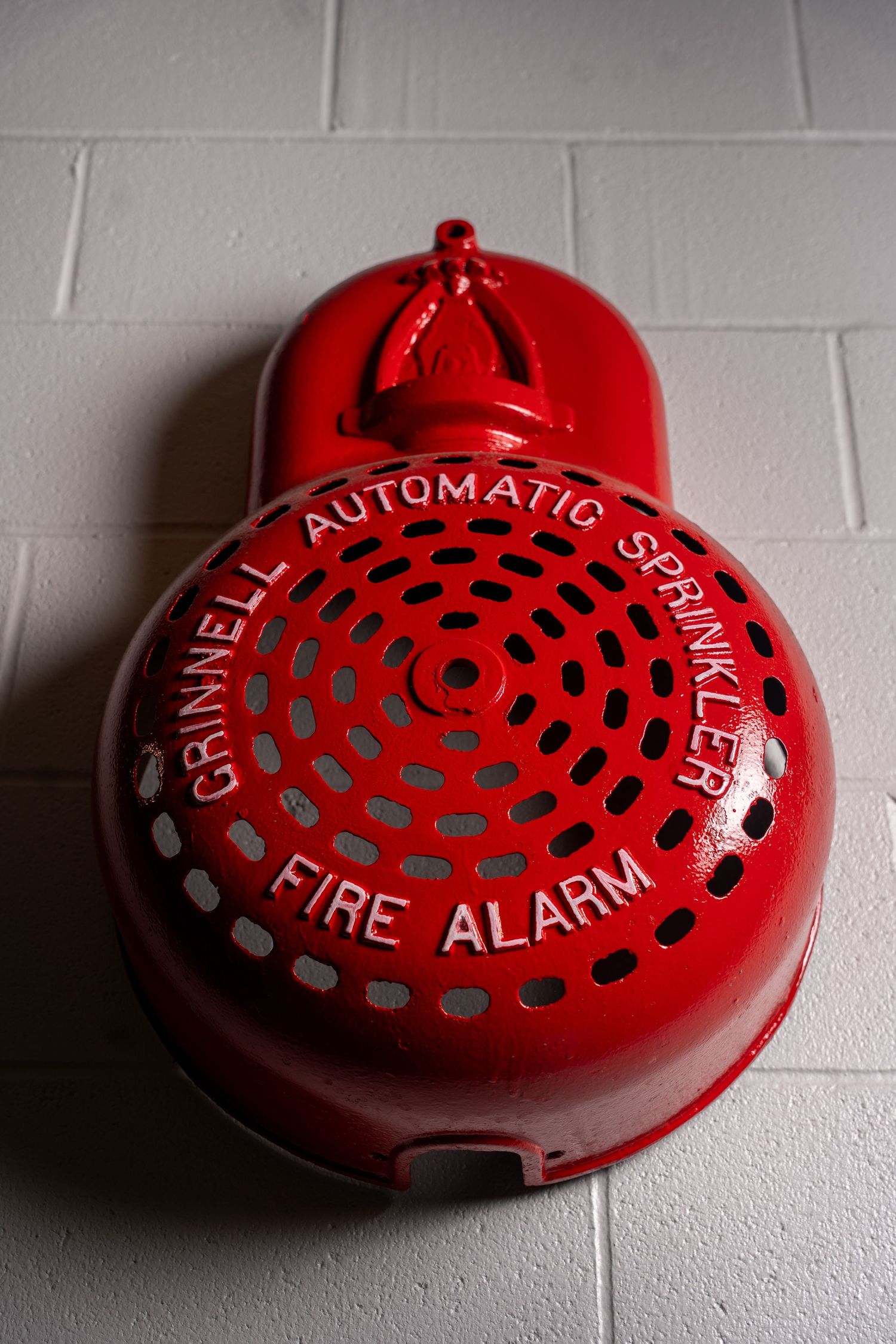 Vintage red Grinnell automatic sprinkler fire alarm bell mounted on a white brick wall.