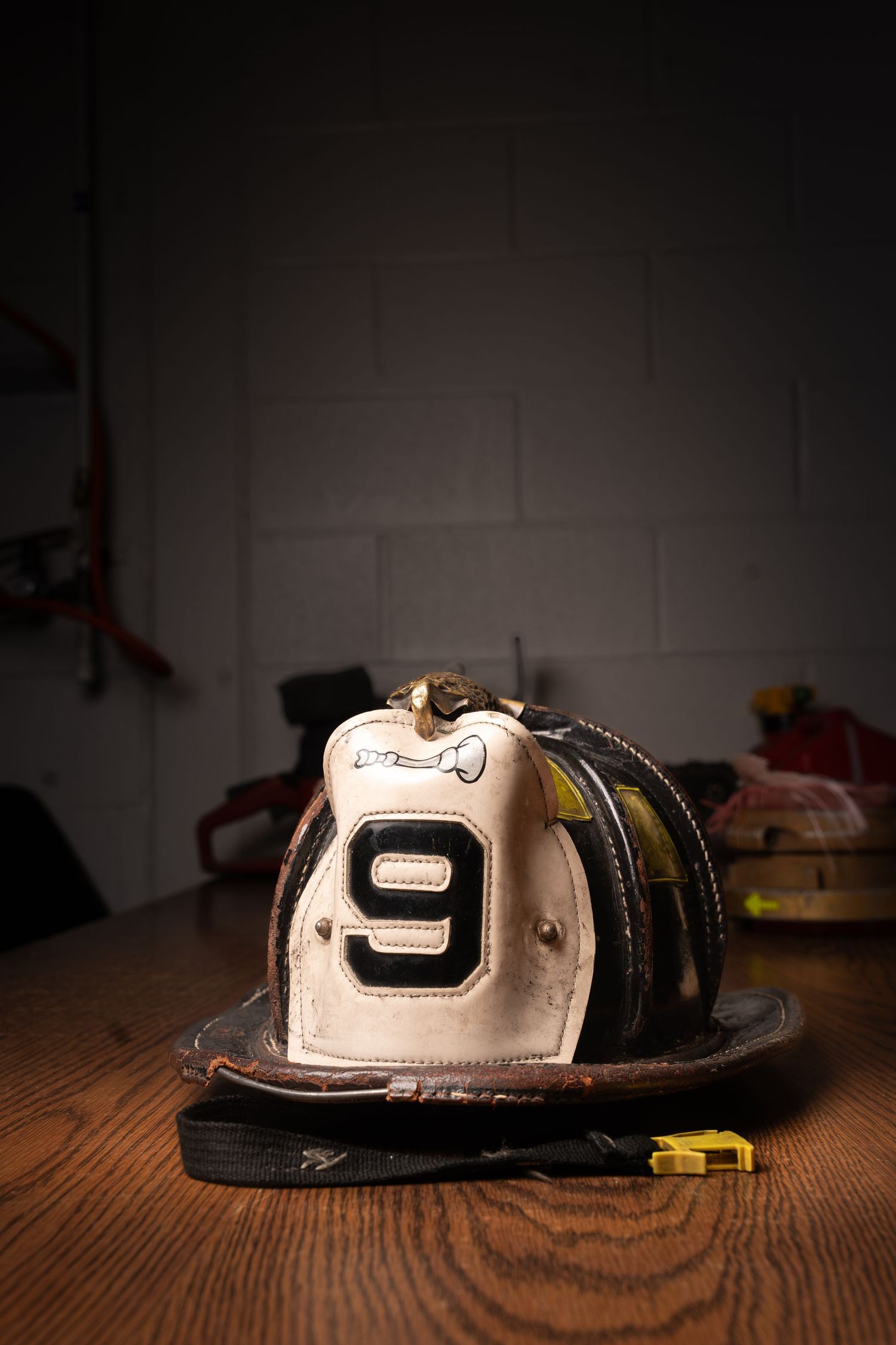 Worn white firefighter helmet with number 9 displayed on front shield, resting on wooden table in dark firehouse.