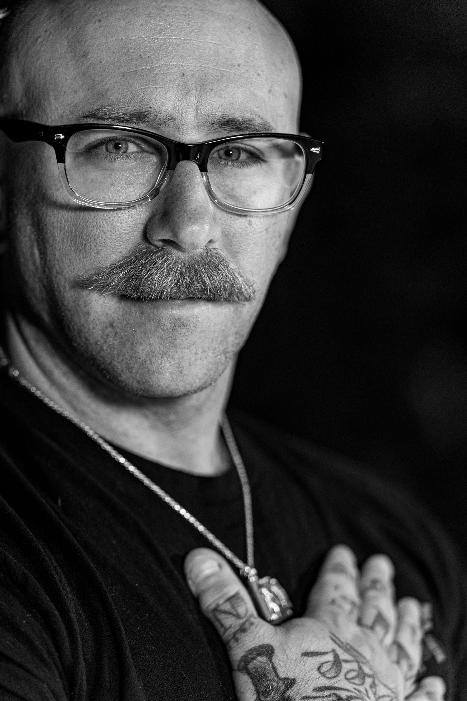 A series of black and white close-up portraits showing glasses, facial hair and hands in dramatic lighting.