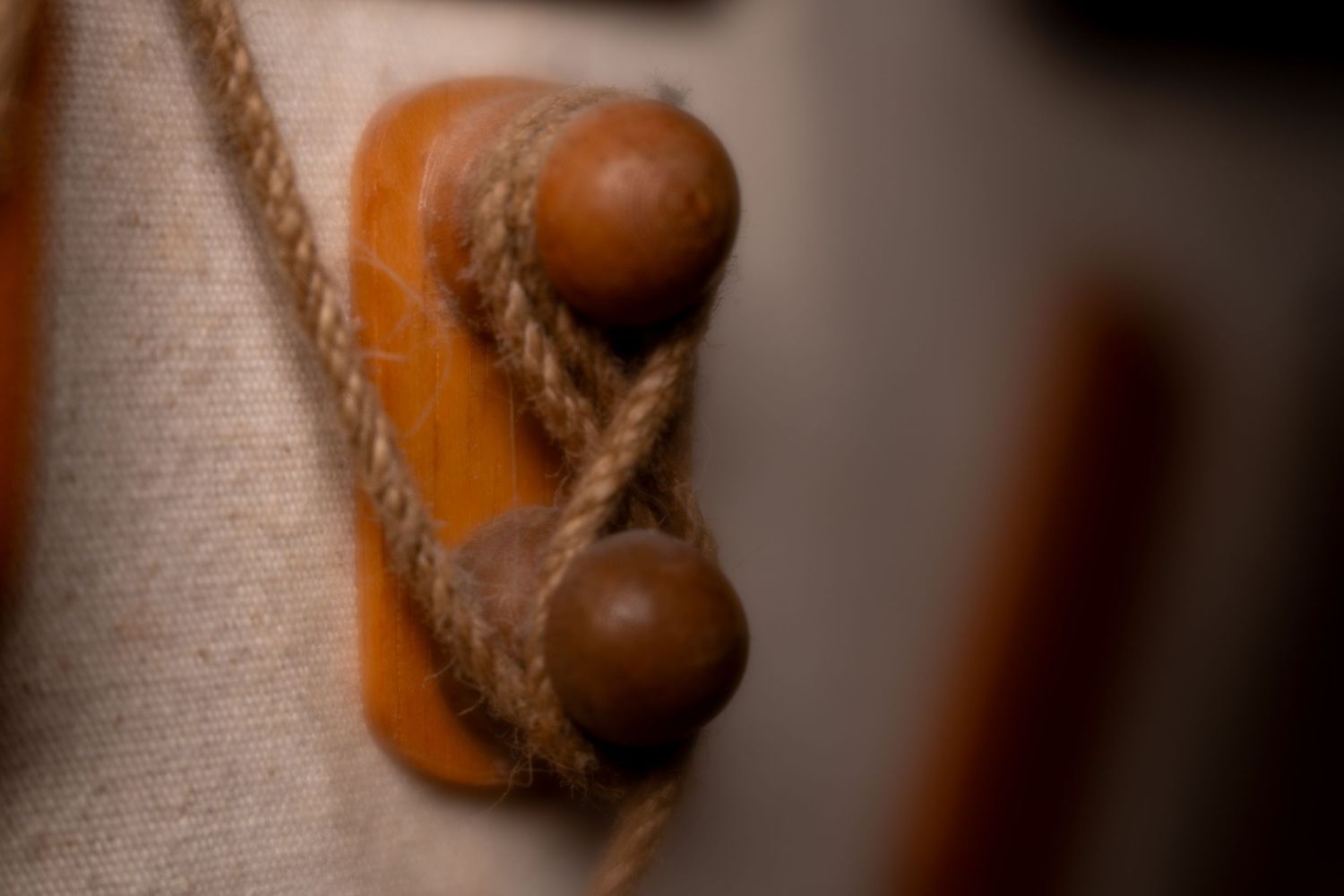 Close-up of a wooden cleat with jute rope tied around two round pegs on a rustic sailboat.
