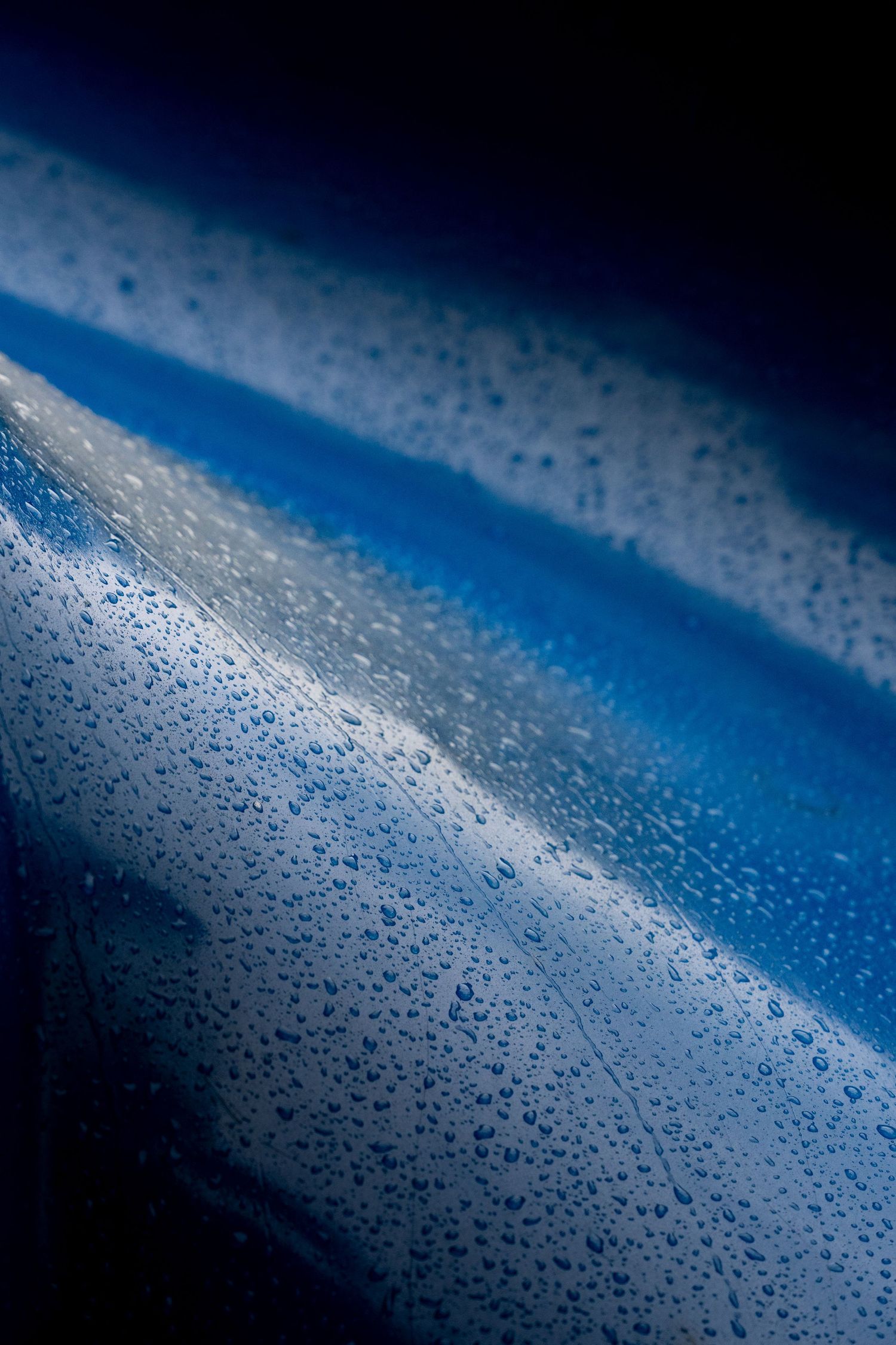 Macro shot of blue curved surface with scattered water droplets against dark background.