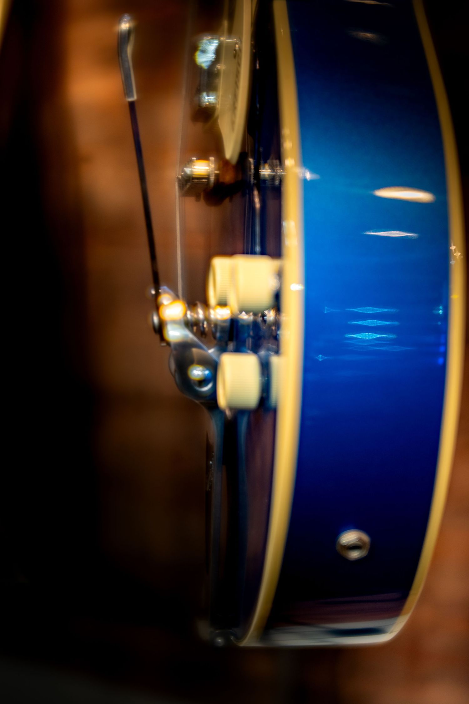 Close-up of a blue electric guitar body showing chrome hardware and tuning mechanisms with warm bokeh background.