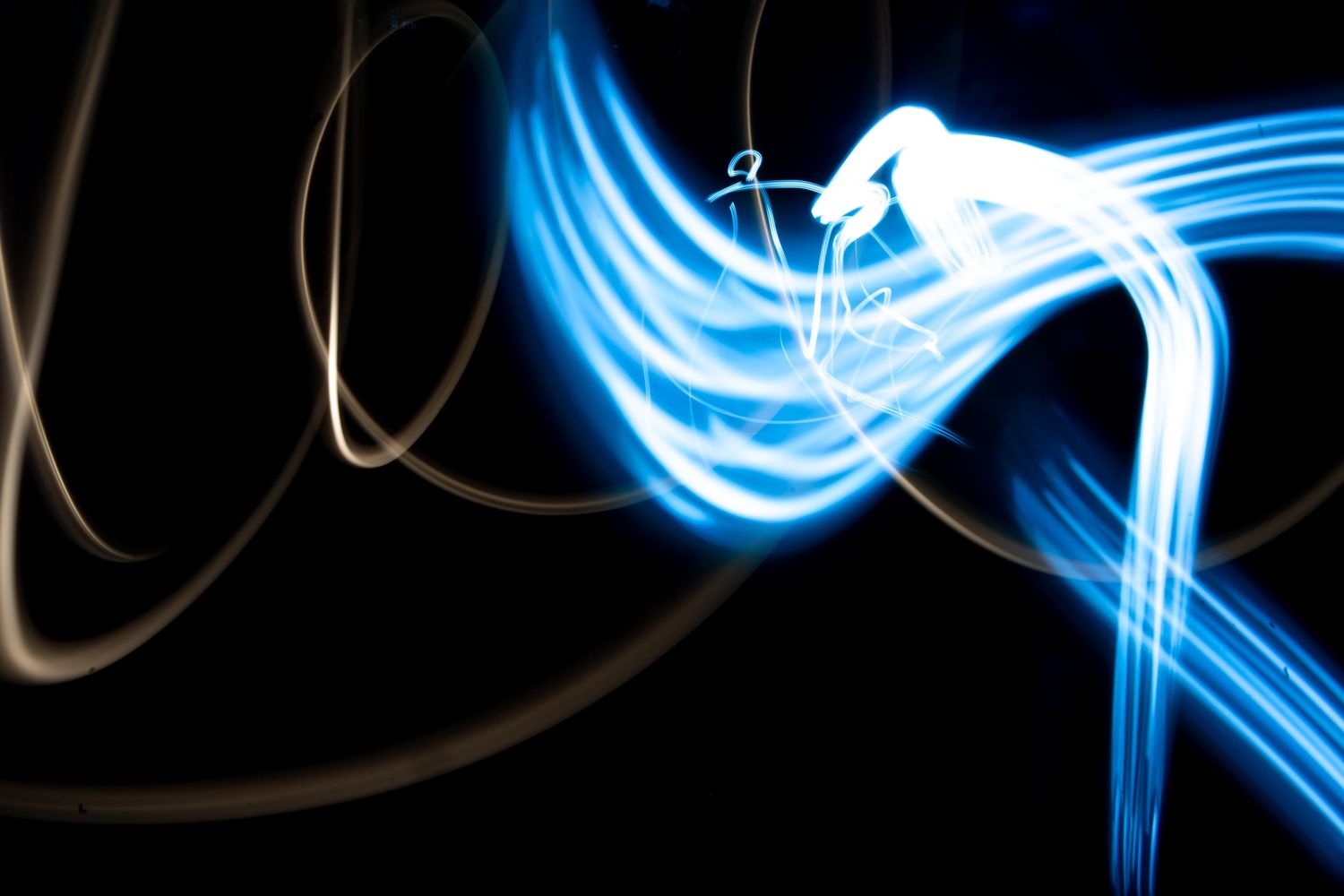 Abstract long exposure light painting photography with glowing blue and white streaks on black background.