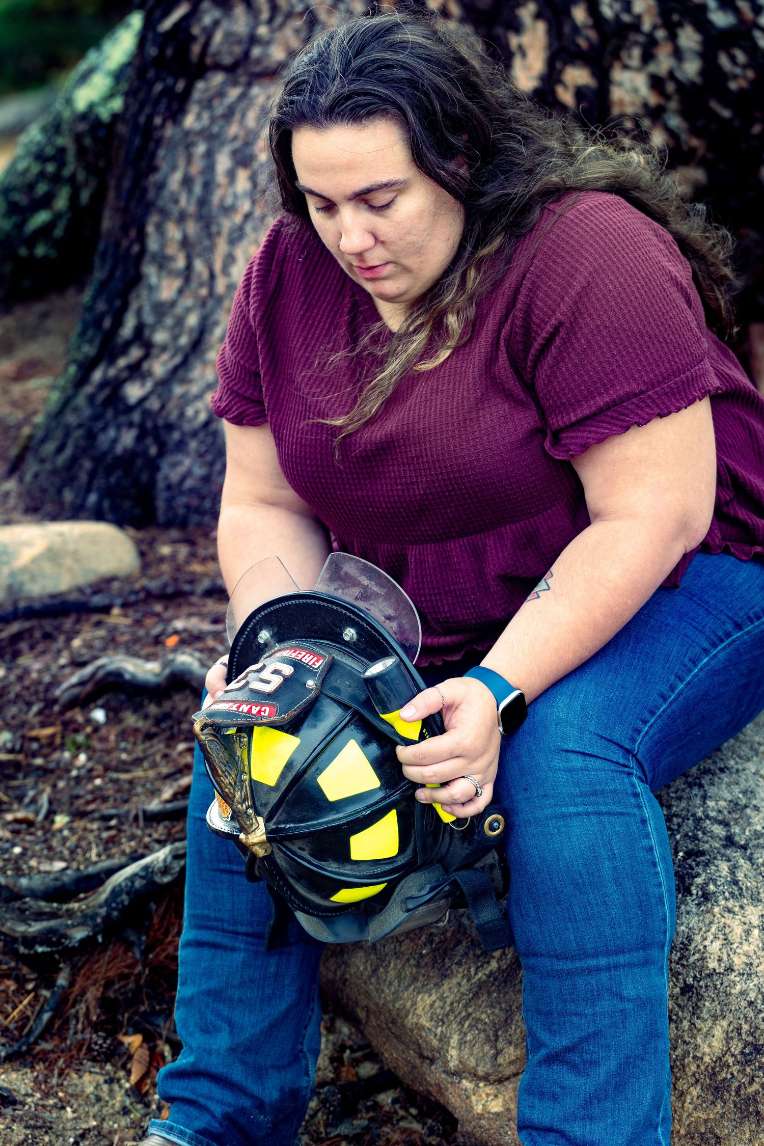 Person in purple sweater and jeans cleaning and maintaining a firefighter helmet outdoors.