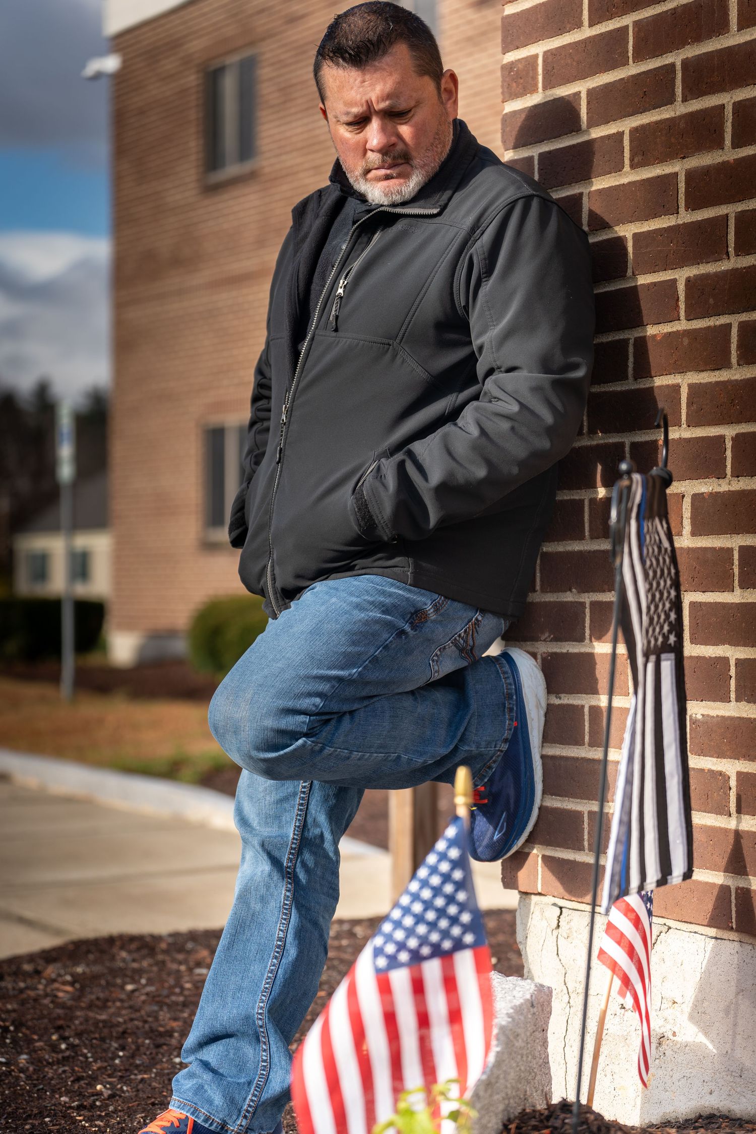 Person in black jacket and jeans sits on brick steps near small American flags.