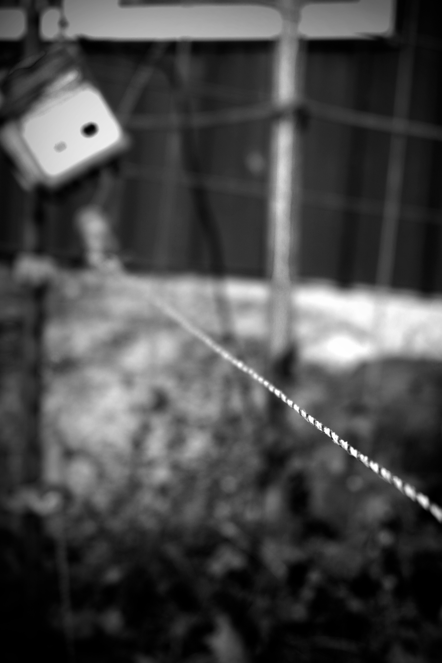 Black and white blurred photo of a twisted wire stretching diagonally with an electrical box mounted on a wall in background.
