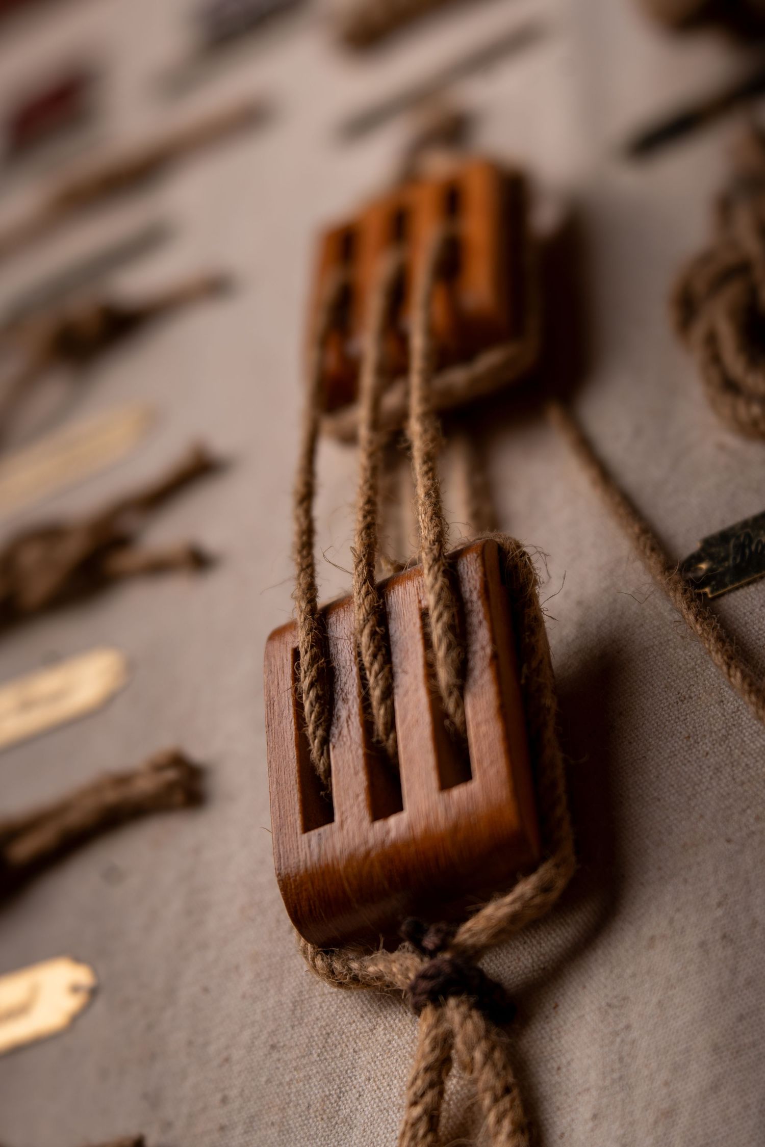 Vintage wooden pulley blocks connected by natural jute rope displayed on a rustic linen surface.
