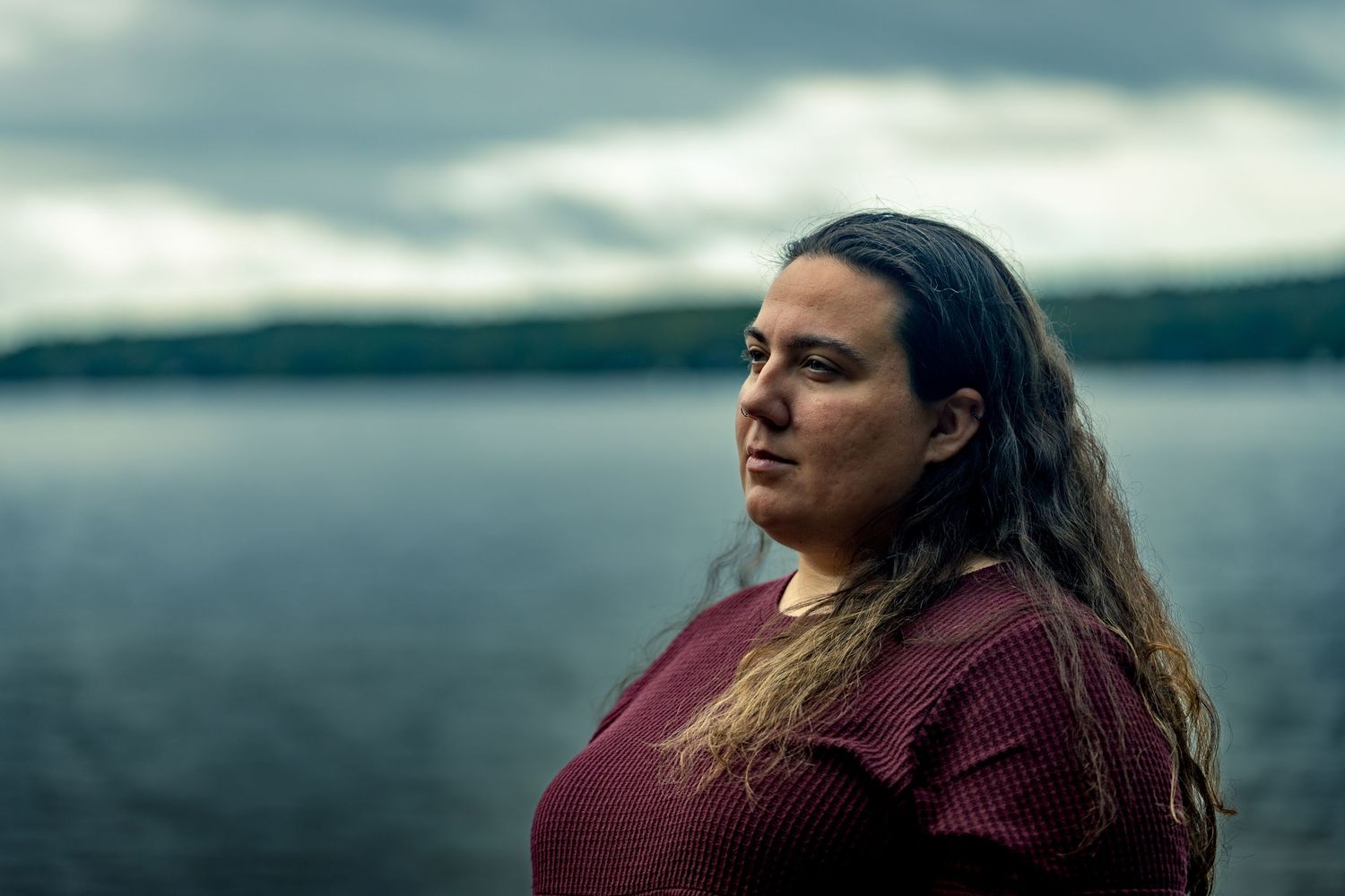 A dramatic portrait of a person in burgundy against a moody cloudy sky backdrop.