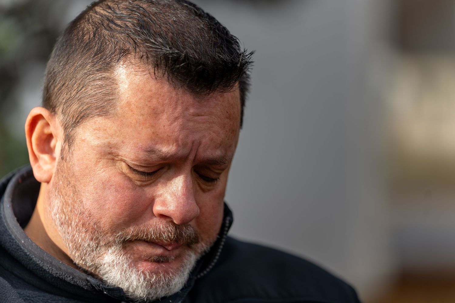 Close-up portrait of a man with gray beard looking down thoughtfully.