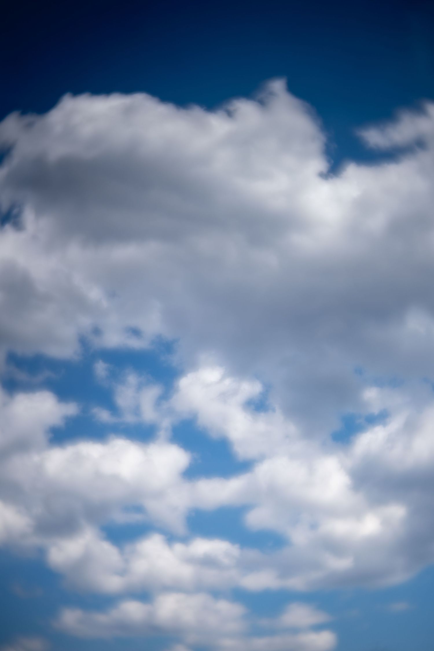 Bright white cumulus clouds drift across a vivid blue sky on a clear sunny day.