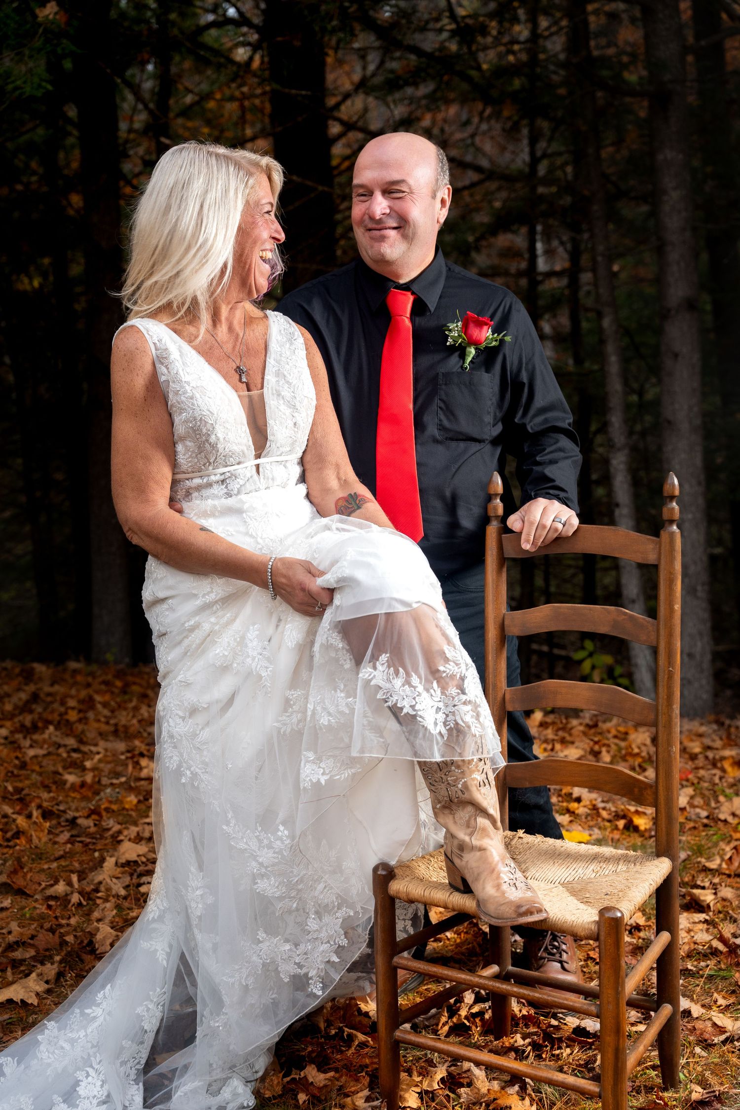 A couple shares a playful moment while sitting on wooden chairs surrounded by autumn leaves in an outdoor setting.