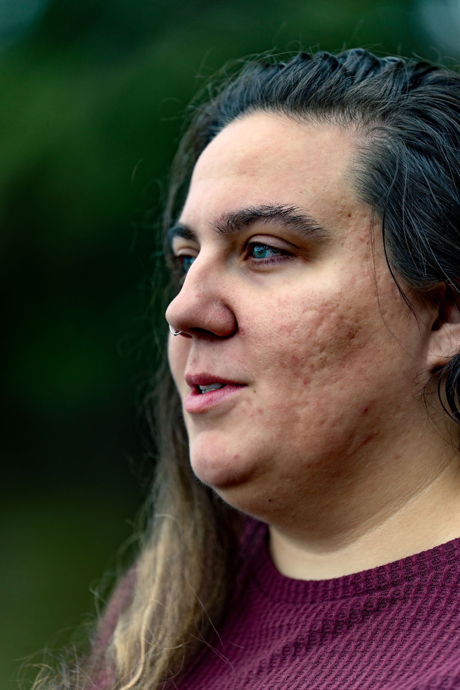 Profile view of person with long brown hair wearing a burgundy sweater against a blurred green background.
