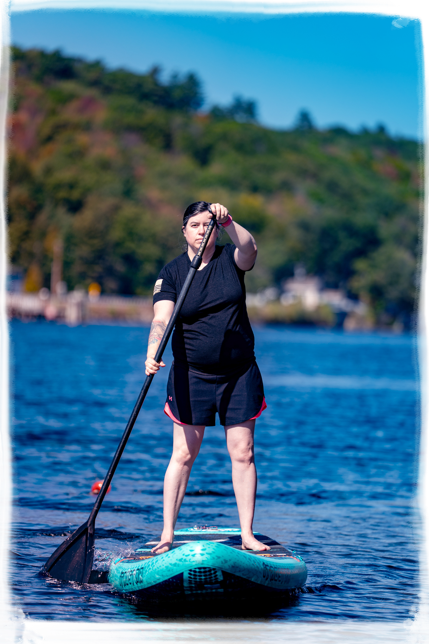 Person paddleboarding on a serene blue lake surrounded by hills on a sunny summer day.