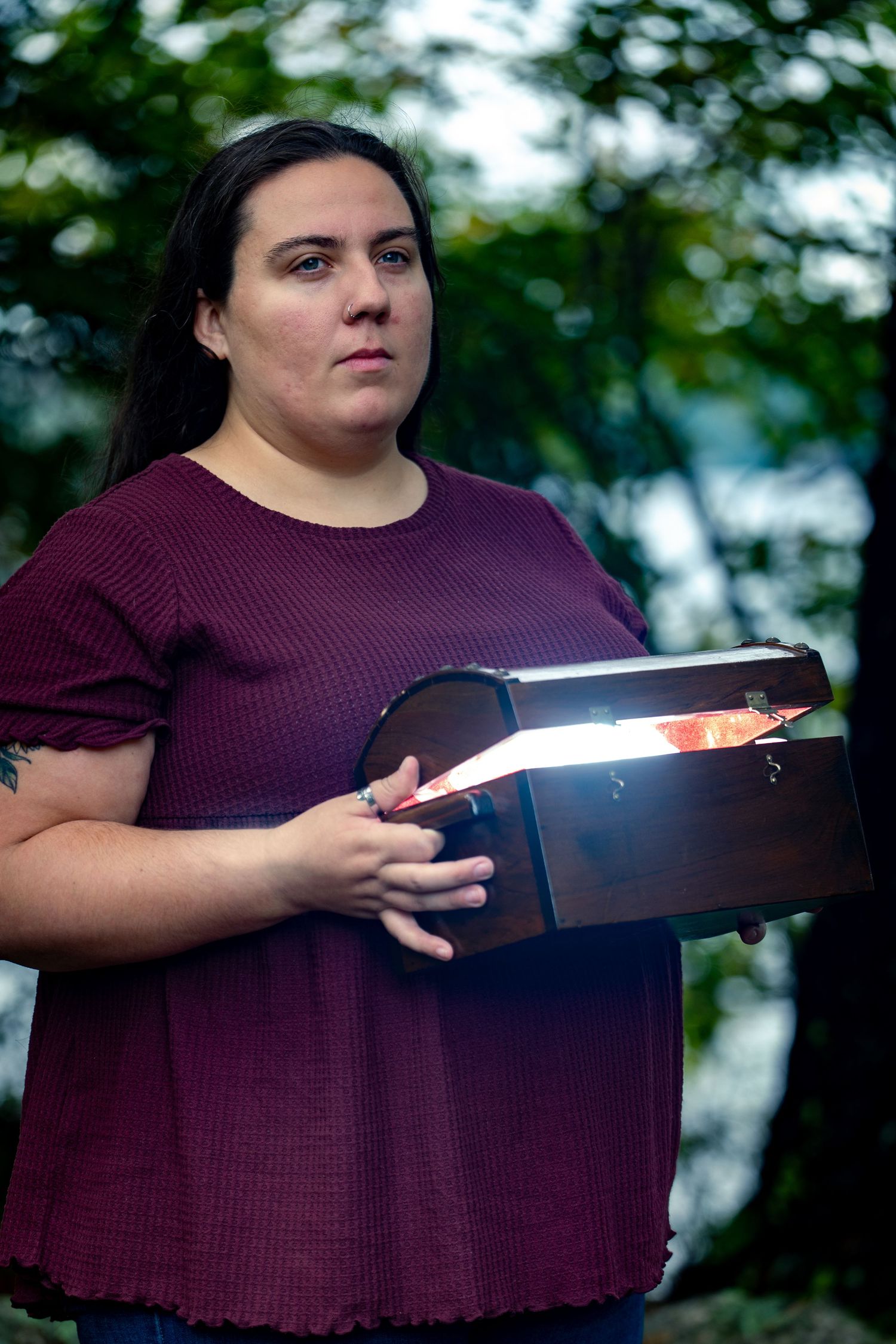 A person in purple holds an illuminated book in an outdoor setting with trees.