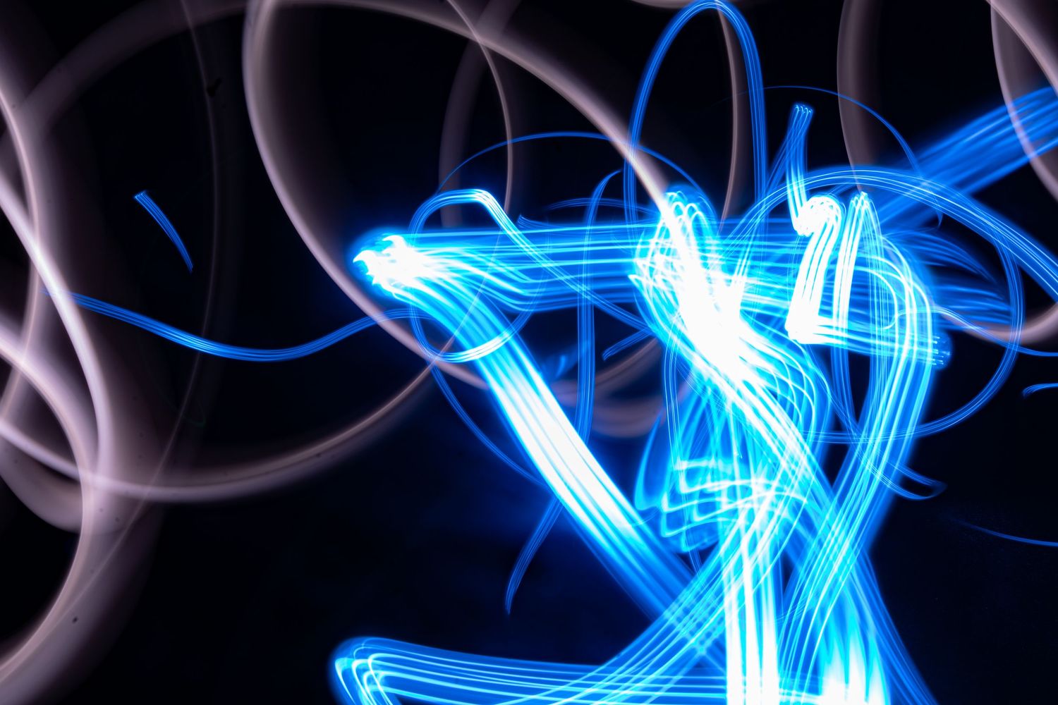 Abstract blue neon light painting on dark background with glowing swirls and human-like figure in long exposure photography.