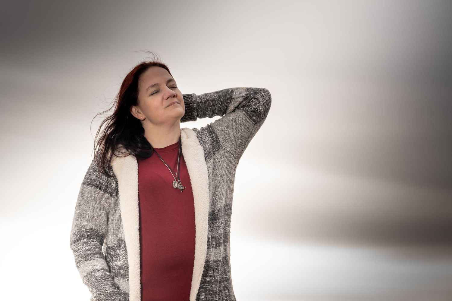Woman in burgundy top and gray cardigan poses in different angles against neutral background.