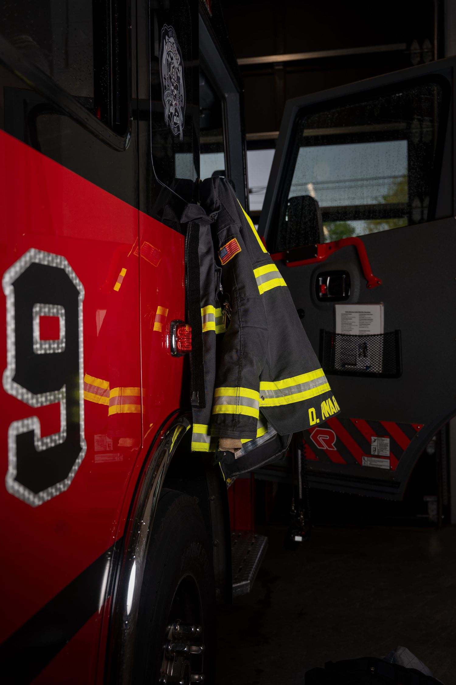 Firefighter turnout gear hanging on a red fire truck door marked with number 9 inside a fire station.